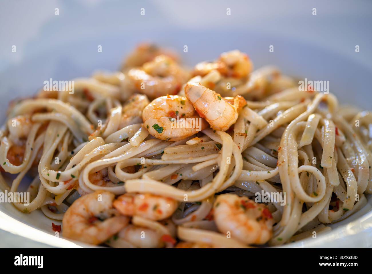 Linguine aglio e olio con gamberi cotti, aglio ed erbe aromatiche servite su un piatto bianco. La pasta è preparata con olio d'oliva e condimento. Foto Stock