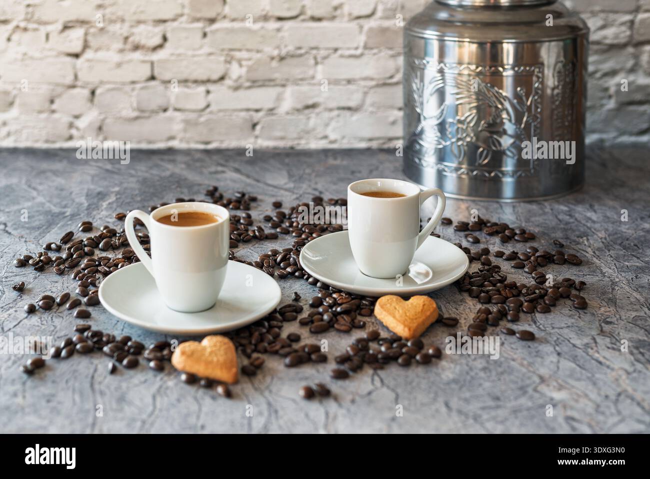 Due tazze da caffè bianche ripiene di caffè appena estratto su piattini circondate da chicchi di caffè tostati. Foto Stock