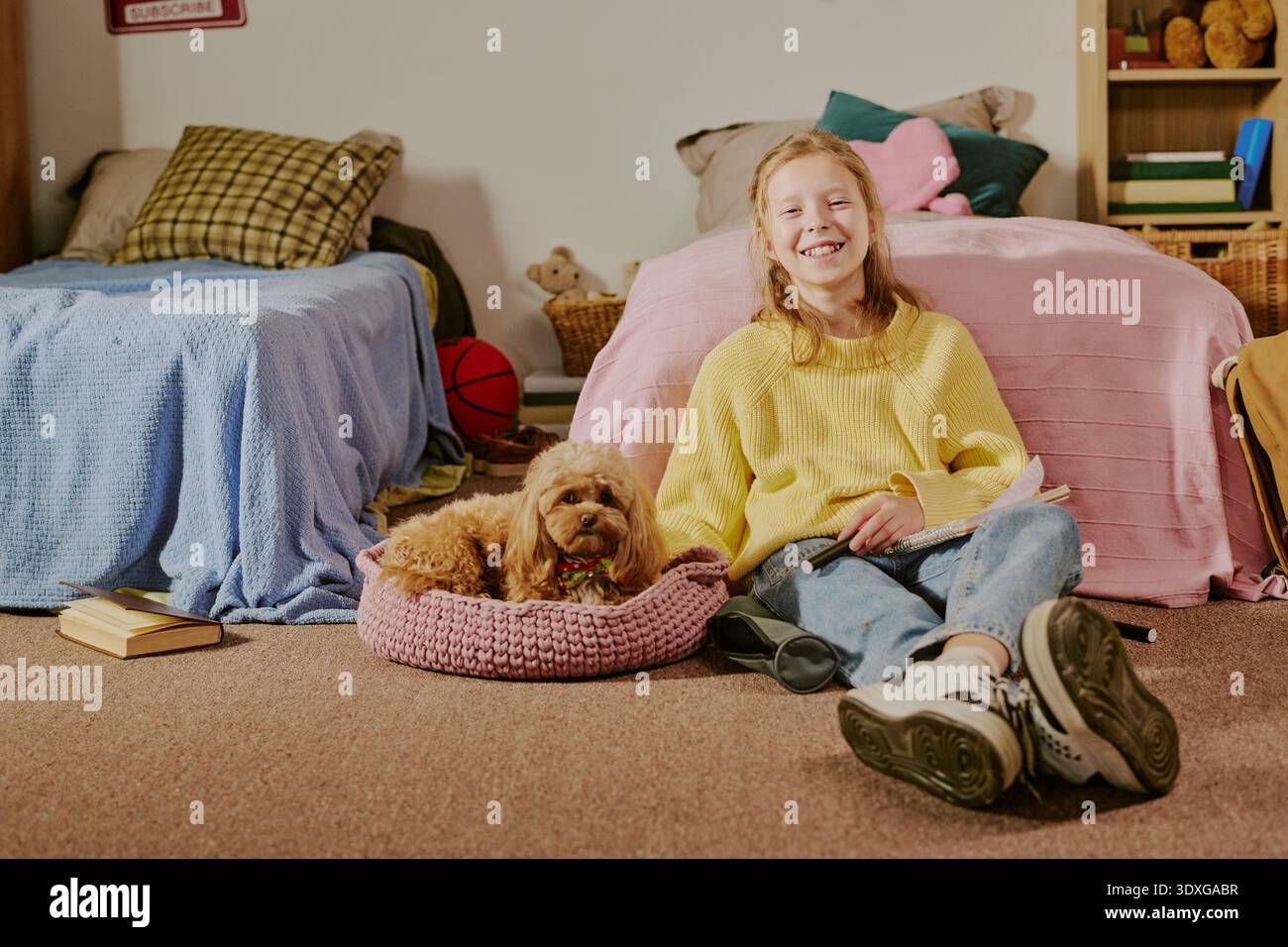 Sorridente ragazza caucasica seduta sul pavimento che legge il libro accanto al cane in casa Foto Stock