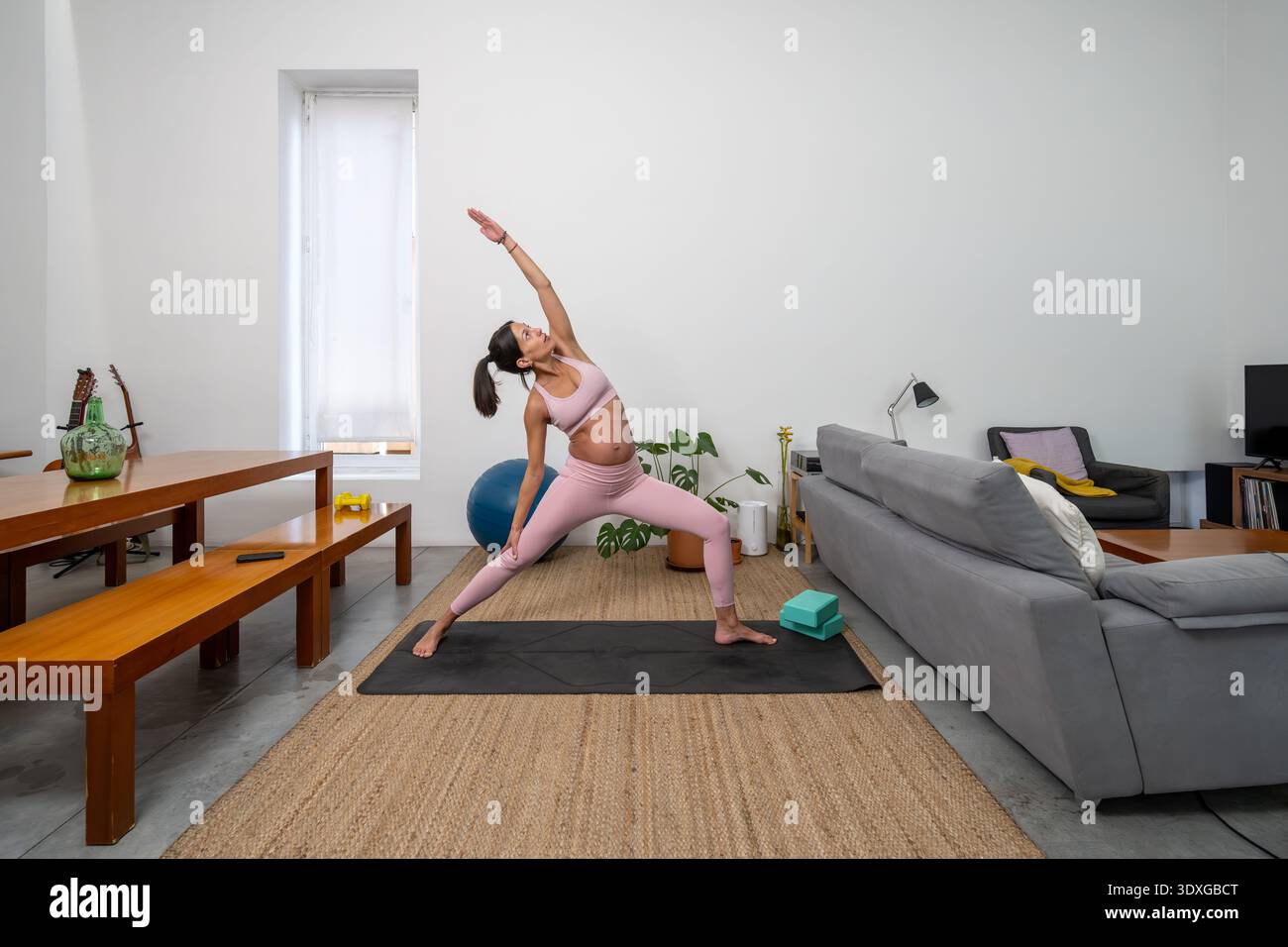 Donna incinta che pratica una posa da guerriera inversa a casa Foto Stock