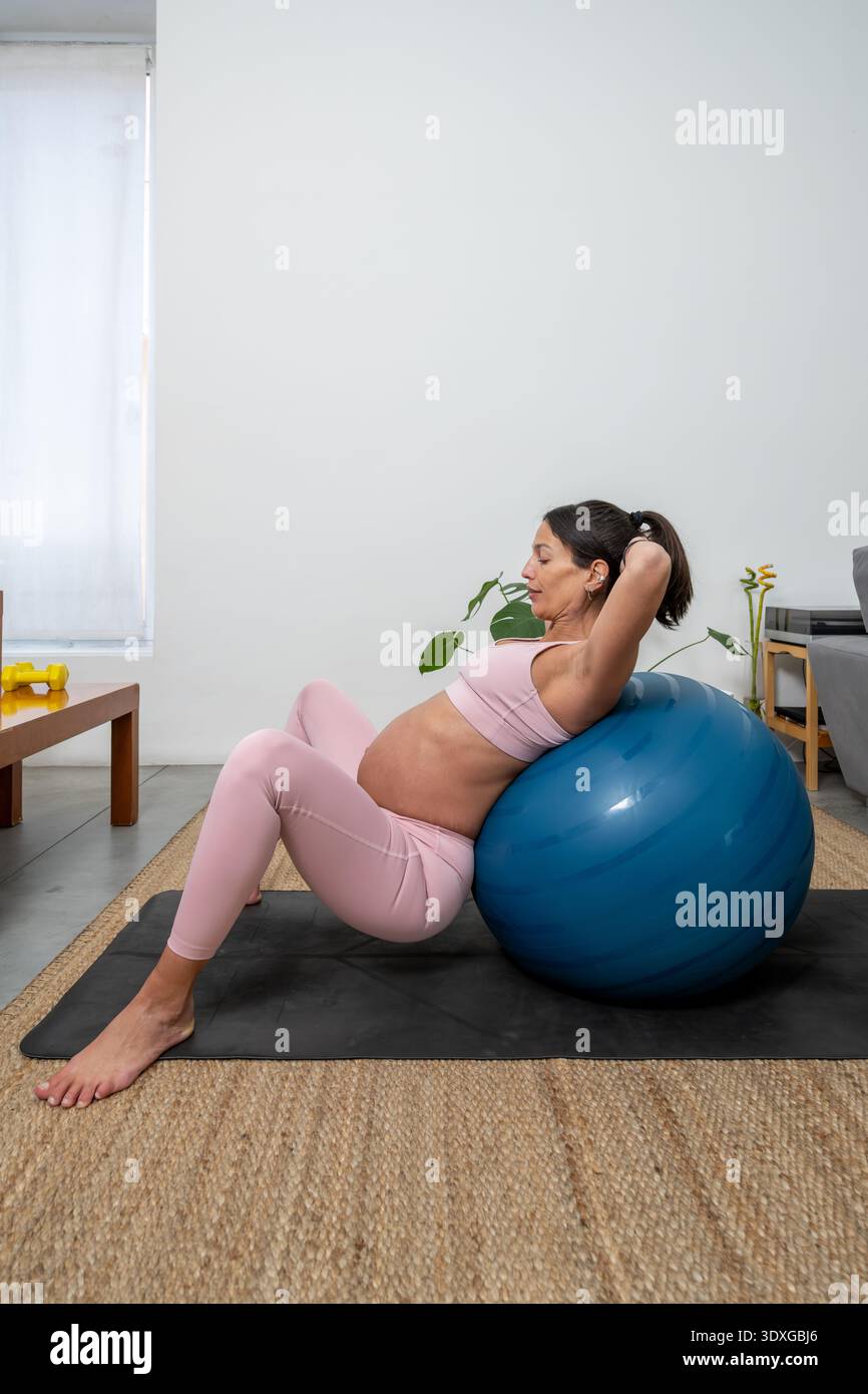 Donna incinta che svolge esercizio di palla di stabilità a HomePregnant Woman Training con palla di esercizio al chiuso Foto Stock