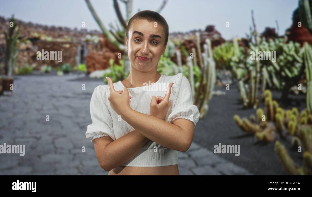 Donna con le braccia tagliate e le dita indice che puntano ai cactus vicini lungo un sentiero lastricato in un giardino di cactus all'aperto con pareti di roccia vulcanica; s Foto Stock