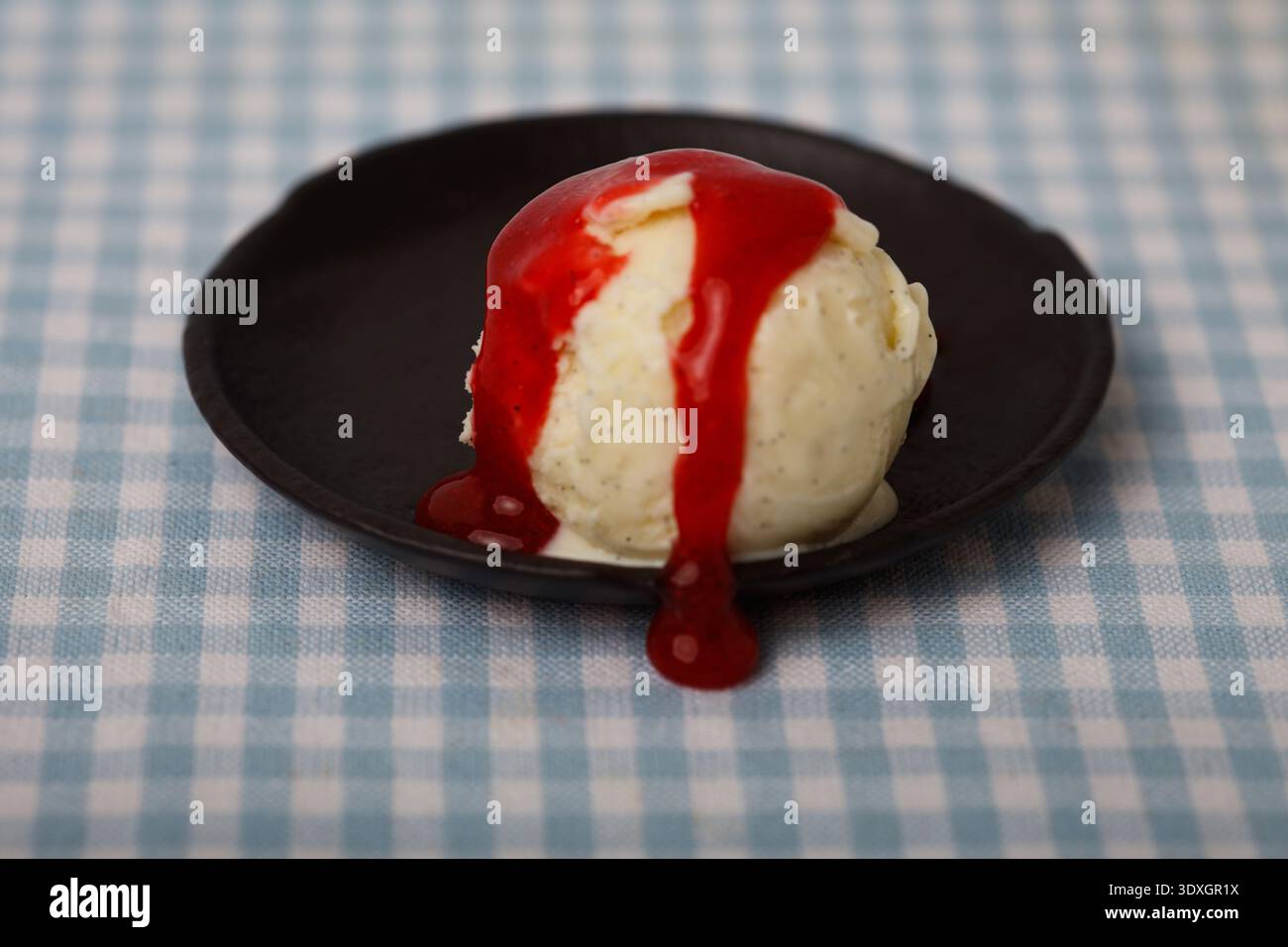 Una sola paletta di gelato di qualità superiore ai chicchi di vaniglia condita con una spessa e lucida salsa di fragole Foto Stock