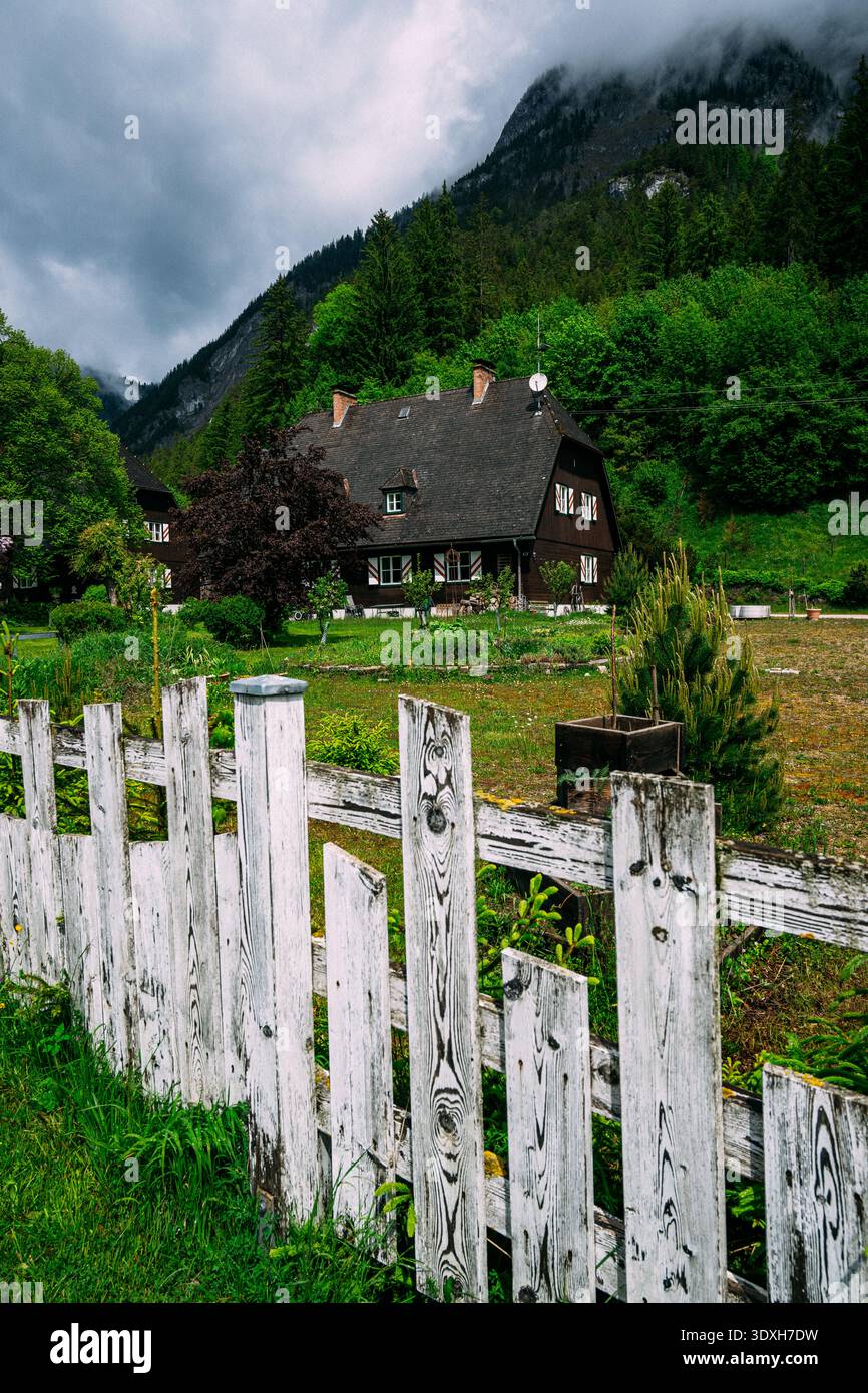Tradizionale casa di legno scuro con recinzione a picchetto bianca e lussureggianti alberi verdi in campagna Foto Stock