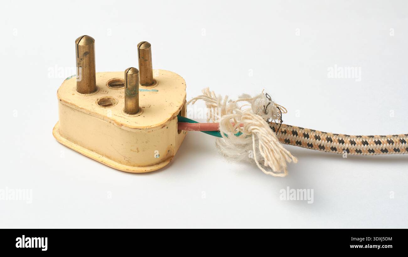 vecchio connettore maschio a tre pin e cavo di alimentazione sfilacciato sfondo bianco isolato, fili interni esposti e guaina intrecciata nera con fibre bianche lacerate Foto Stock