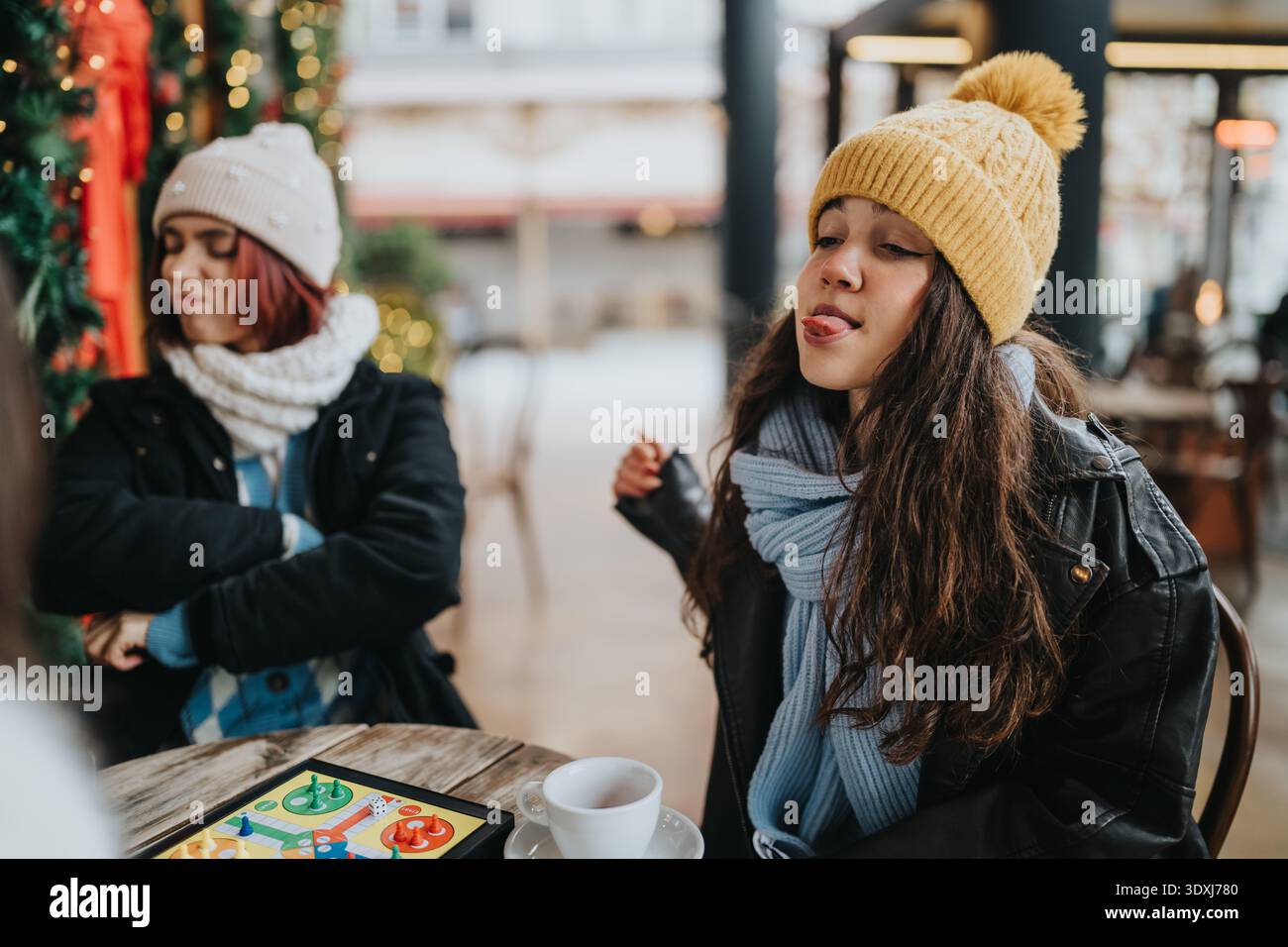 Due ragazze con abiti invernali si godono un momento di caffe' con un gioco da tavolo e un caffe' Foto Stock