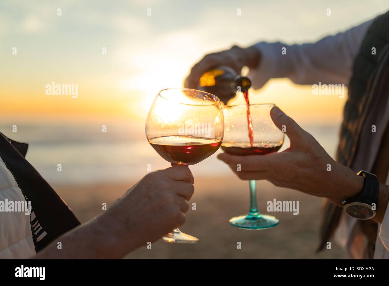 Versare vino rosso nei bicchieri durante il tramonto sulla spiaggia Foto Stock