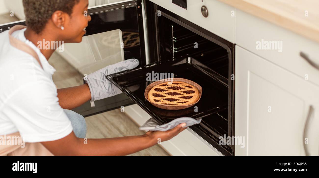 La donna posiziona una torta nel forno della cucina durante la sessione di cottura pomeridiana Foto Stock