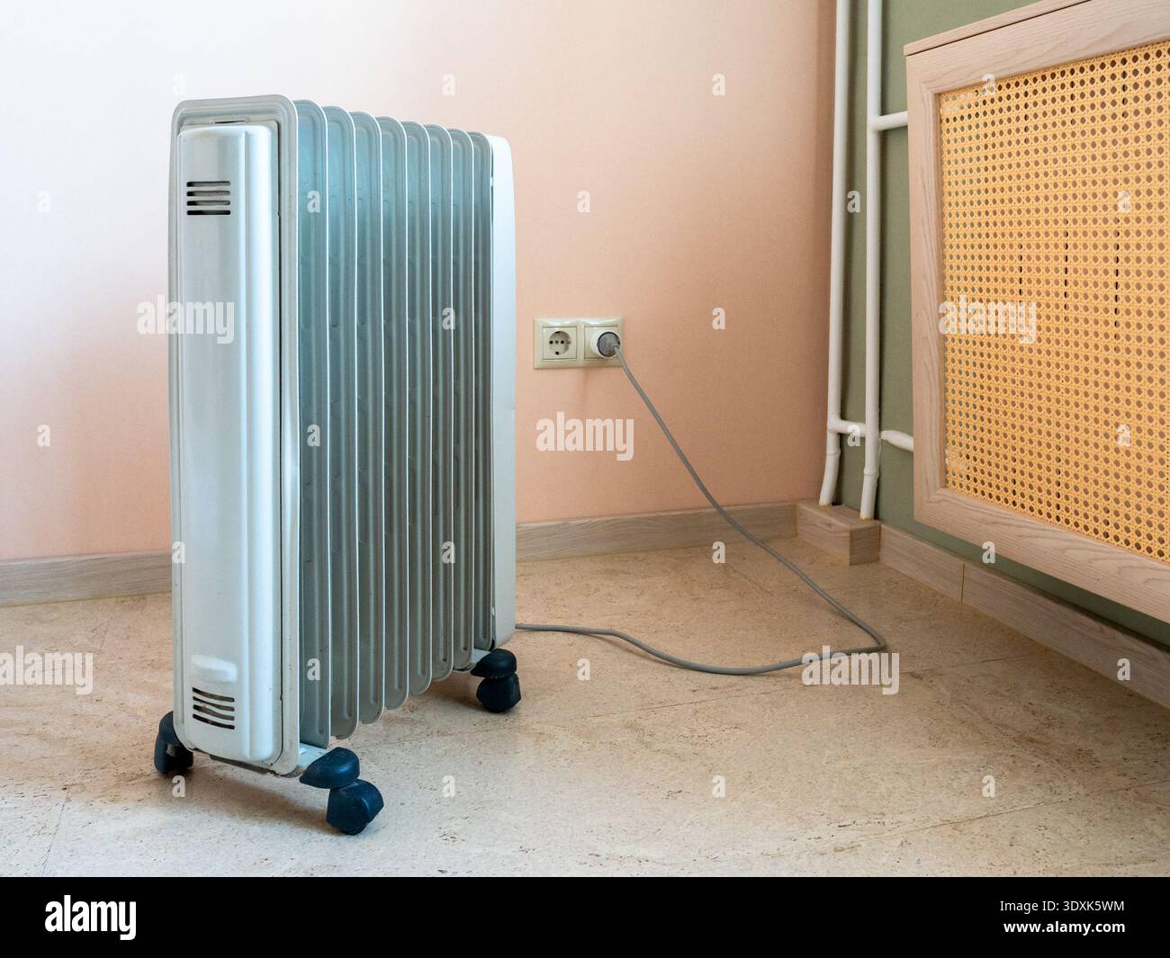 riscaldamento elettrico a olio e radiatore di riscaldamento coperto con schermo paglia nella stanza dell'appartamento residenziale Foto Stock