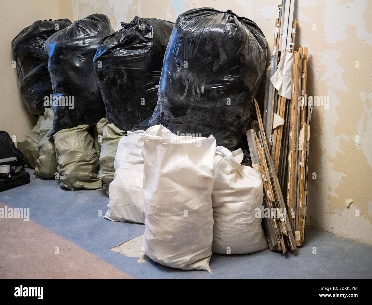pile di sacchi con rifiuti di costruzione contro la parete della stanza con carta da parati staccata durante la ristrutturazione dell'appartamento Foto Stock