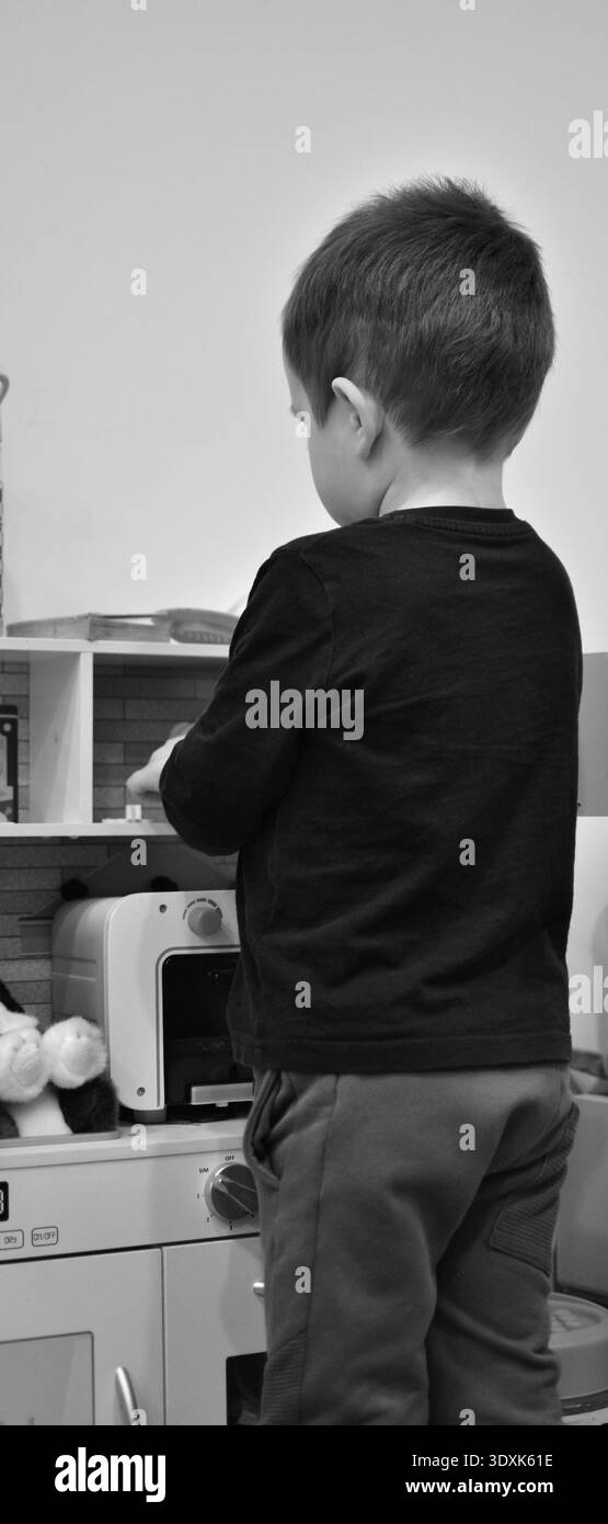Bambino che gioca con il giocattolo da cucina a casa, fingendo di cucinare. Scena di vita al chiuso con giocattoli educativi, sviluppo dell'immaginazione e creazione Foto Stock
