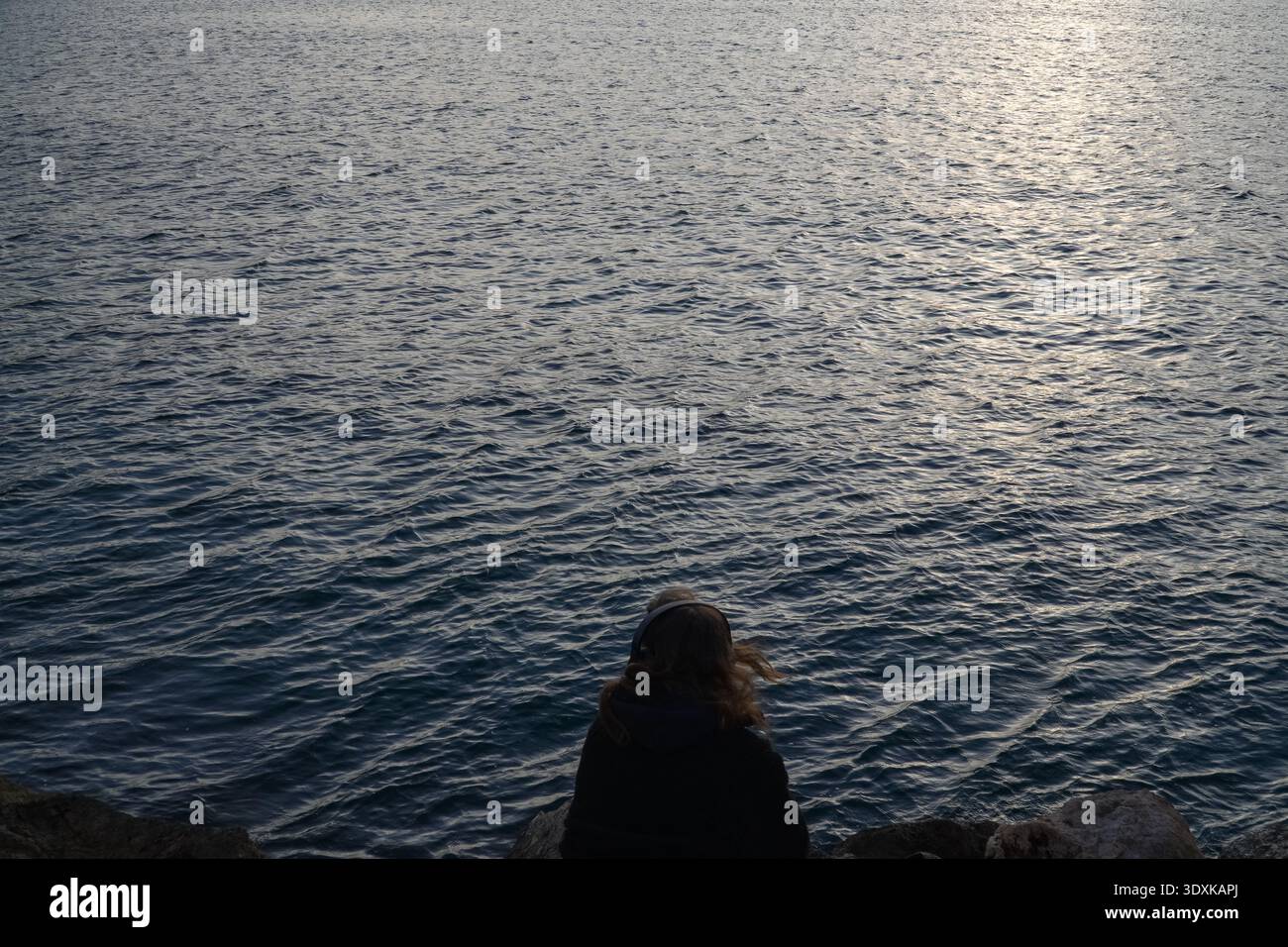 Donna con cuffie sedute sulle rocce che si affaccia sul Mar Mediterraneo a Marsiglia, Francia. Contemplazione, ascolto di musica, vista mare. Foto Stock