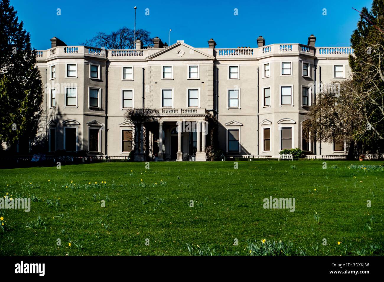 Facciata anteriore della Farmleigh House nel Phoenix Park, Dublino, Irlanda. La grande tenuta d'epoca si trova dietro un prato verde con narcisi gialli. Foto Stock