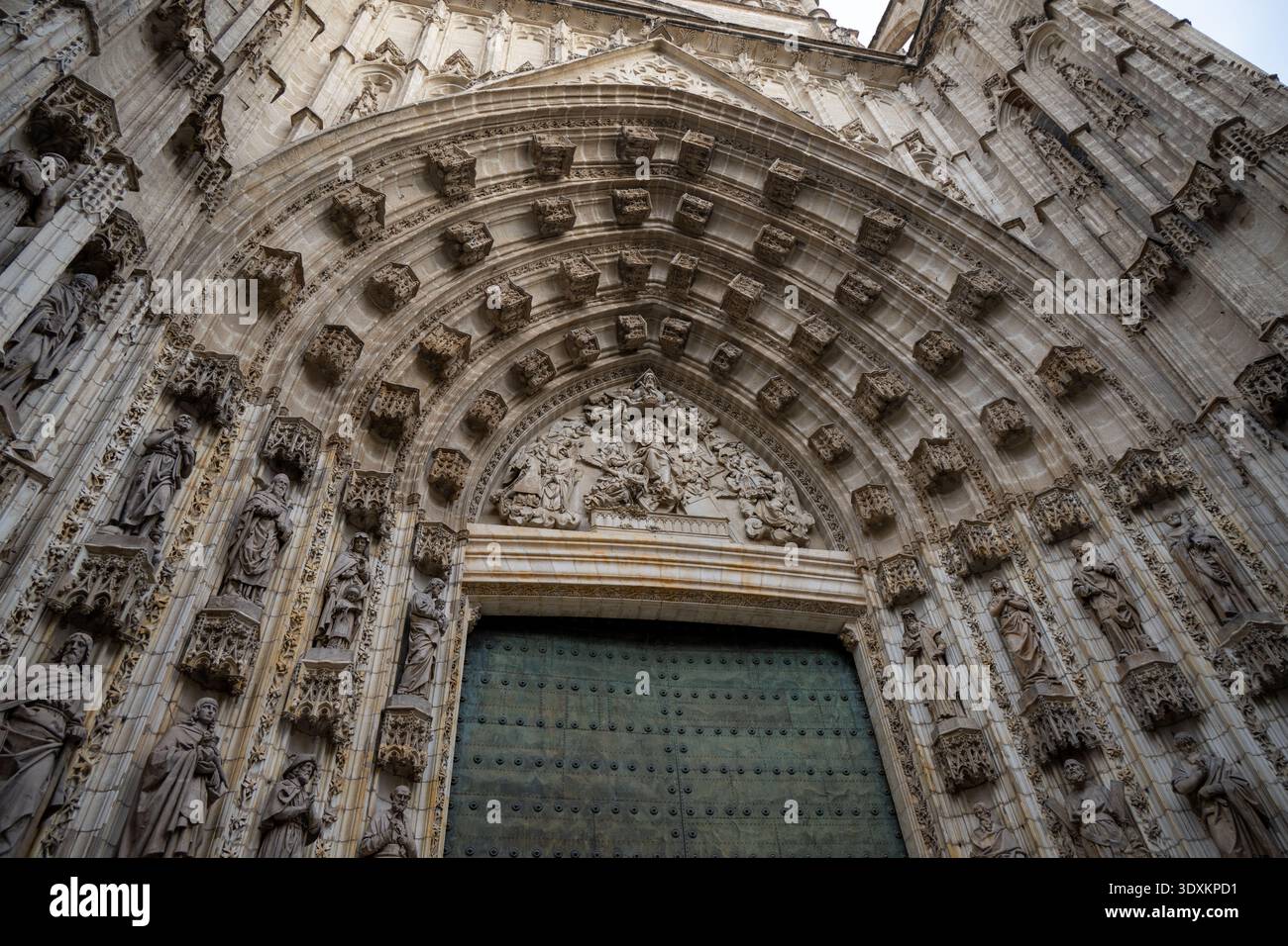 Vista ad angolo basso di una grande cattedrale gotica con arco in pietra scolpita e grande porta a Siviglia, Andalusia, Spagna. Dettagli architettonici spettacolari Foto Stock