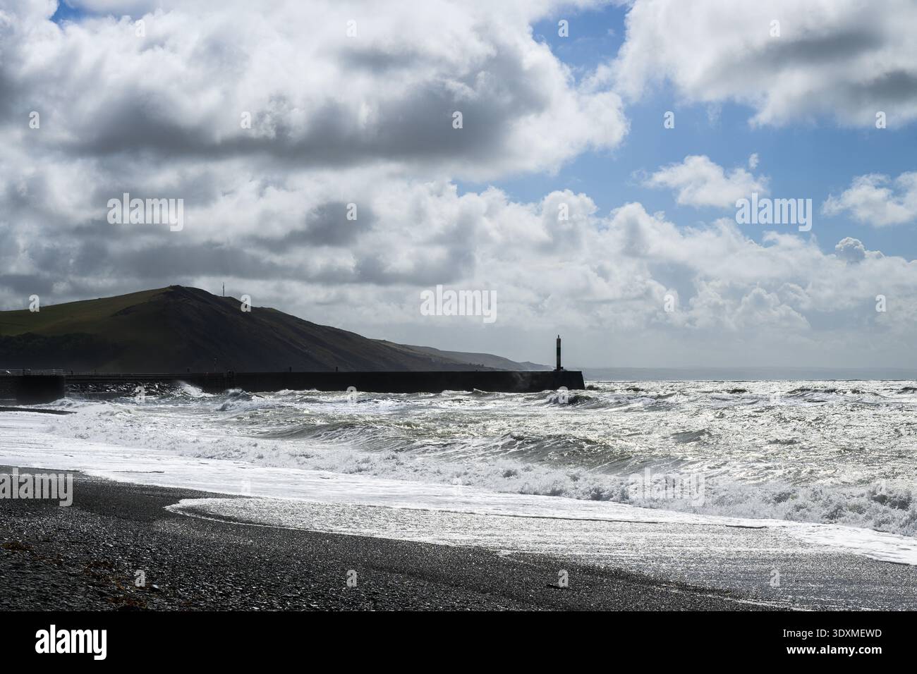 Vista a sud verso Aberystwyth Harbour Light sotto il cielo luminoso e soleggiato con mare frastagliato Foto Stock