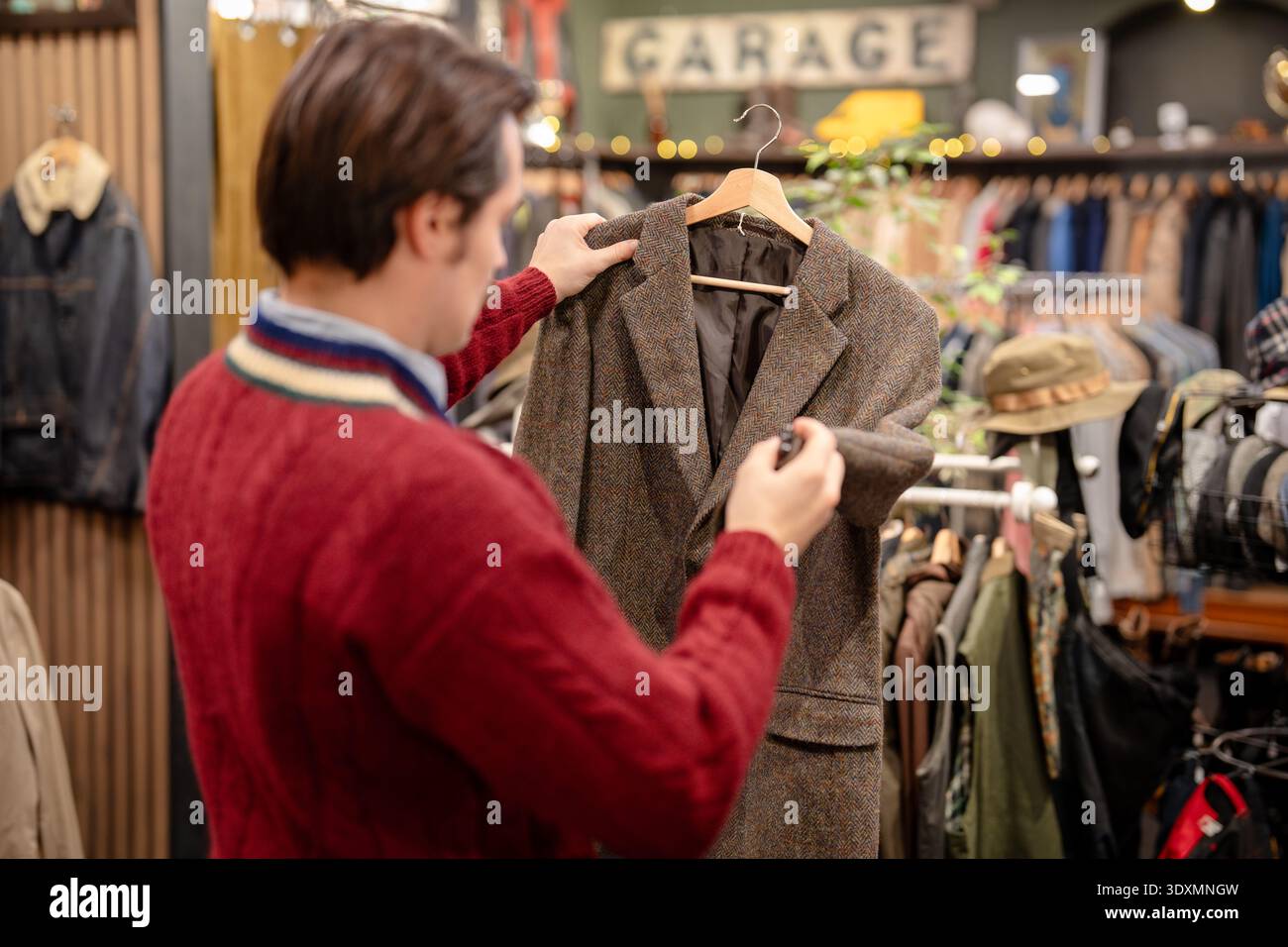 Uomo hipster che ispeziona la qualità della giacca usata alla moda nel negozio vintage di abbigliamento maschile alla moda. Foto Stock