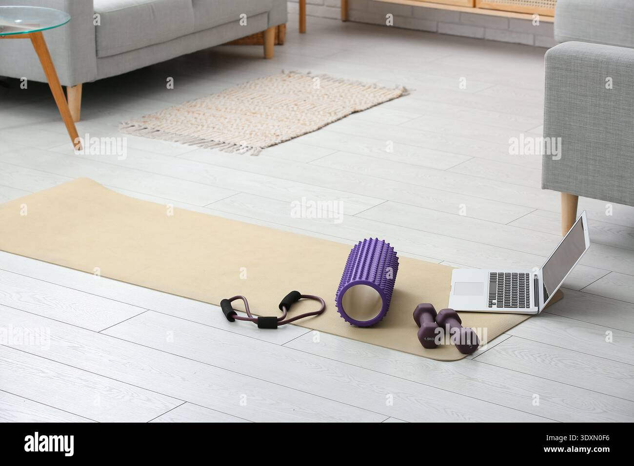 Rullo in gommapiuma con laptop, manubri e dilatatore per il fitness sul tappetino yoga nel soggiorno Foto Stock