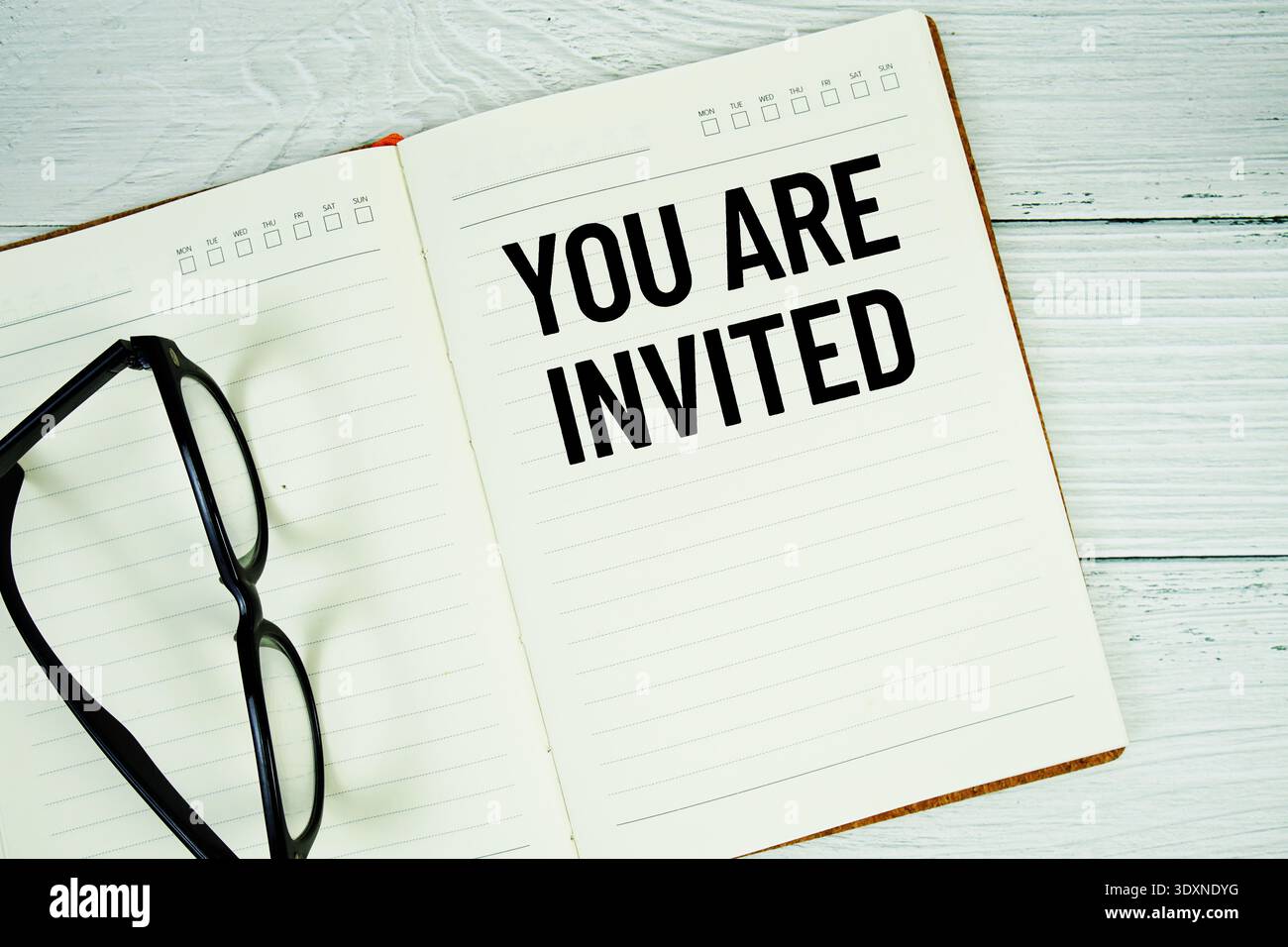 Blocco note con messaggio "siete invitati" e occhiali su sfondo in legno Foto Stock