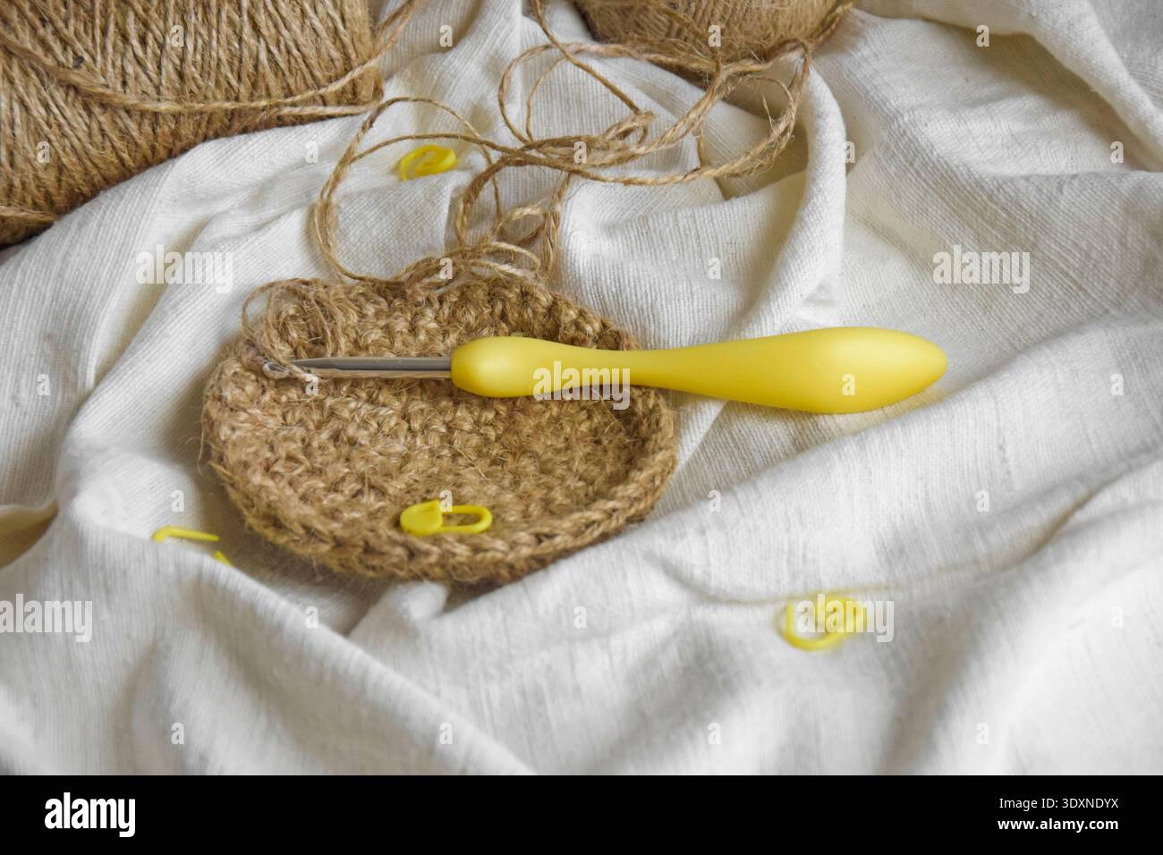 Lavoro di manifattura. Fibra di iuta naturale, gancio per maglieria giallo e spille su tessuto leggero. Processo iniziale del cestello di juta. Copia spazio Foto Stock