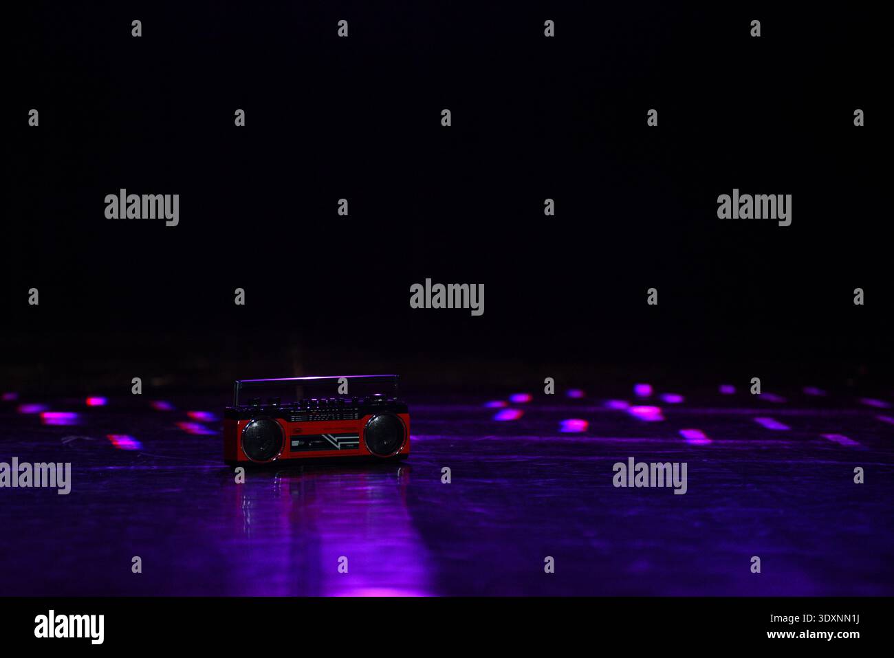 Stereo portatile rosso vintage posizionato su un palcoscenico scuro riflettente illuminato da luci al neon viola. Scena minimalista con spazio per le copie, ideale per la musica e la notte Foto Stock