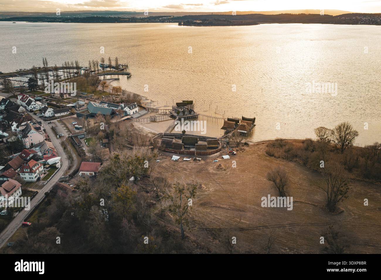 Ampia vista con un lago, tradizionali palafitte e calda luce del tramonto, palafitte Unteruhldingen, Bodenseekreis, Germania Foto Stock