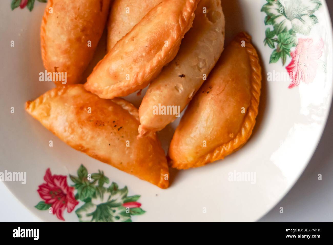 Sei soffioni di curry dorati disposti su piatto floreale con design decorativo. Foto Stock