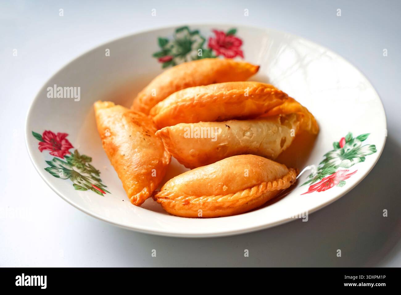 Sei soffioni di curry dorati disposti su piatto floreale con design decorativo. Foto Stock
