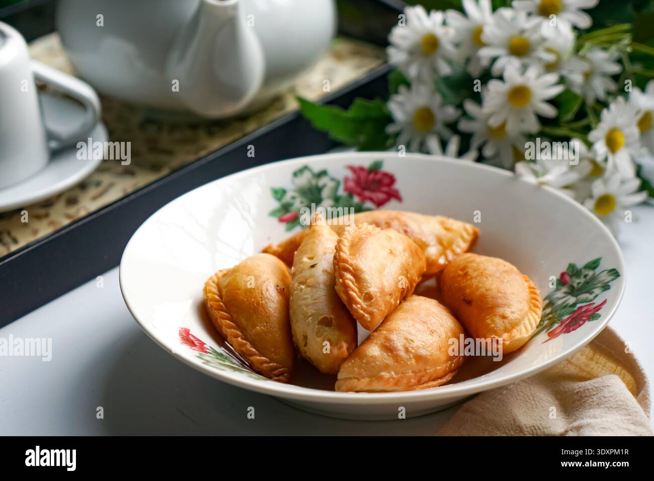 Un piatto di spugne di curry dorate con set da tè e margherite su sfondo bianco. Foto Stock