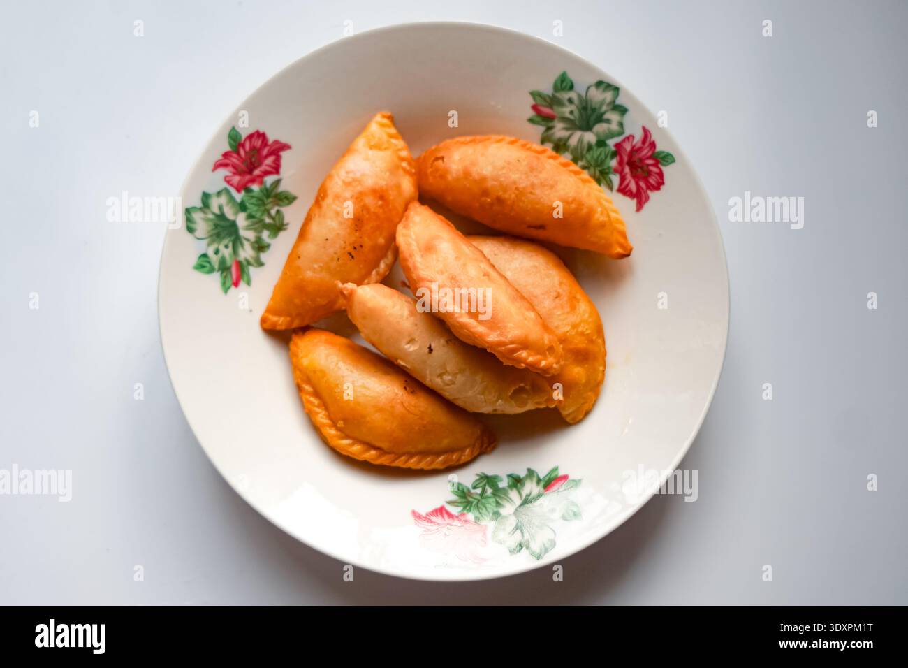 Sei soffioni di curry dorati disposti su piatto floreale con design decorativo. Foto Stock
