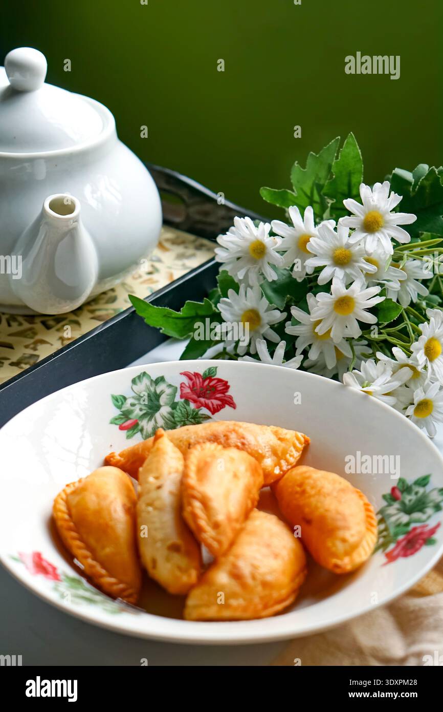 Un piatto di spugne di curry dorate con set da tè e margherite su sfondo bianco. Foto Stock
