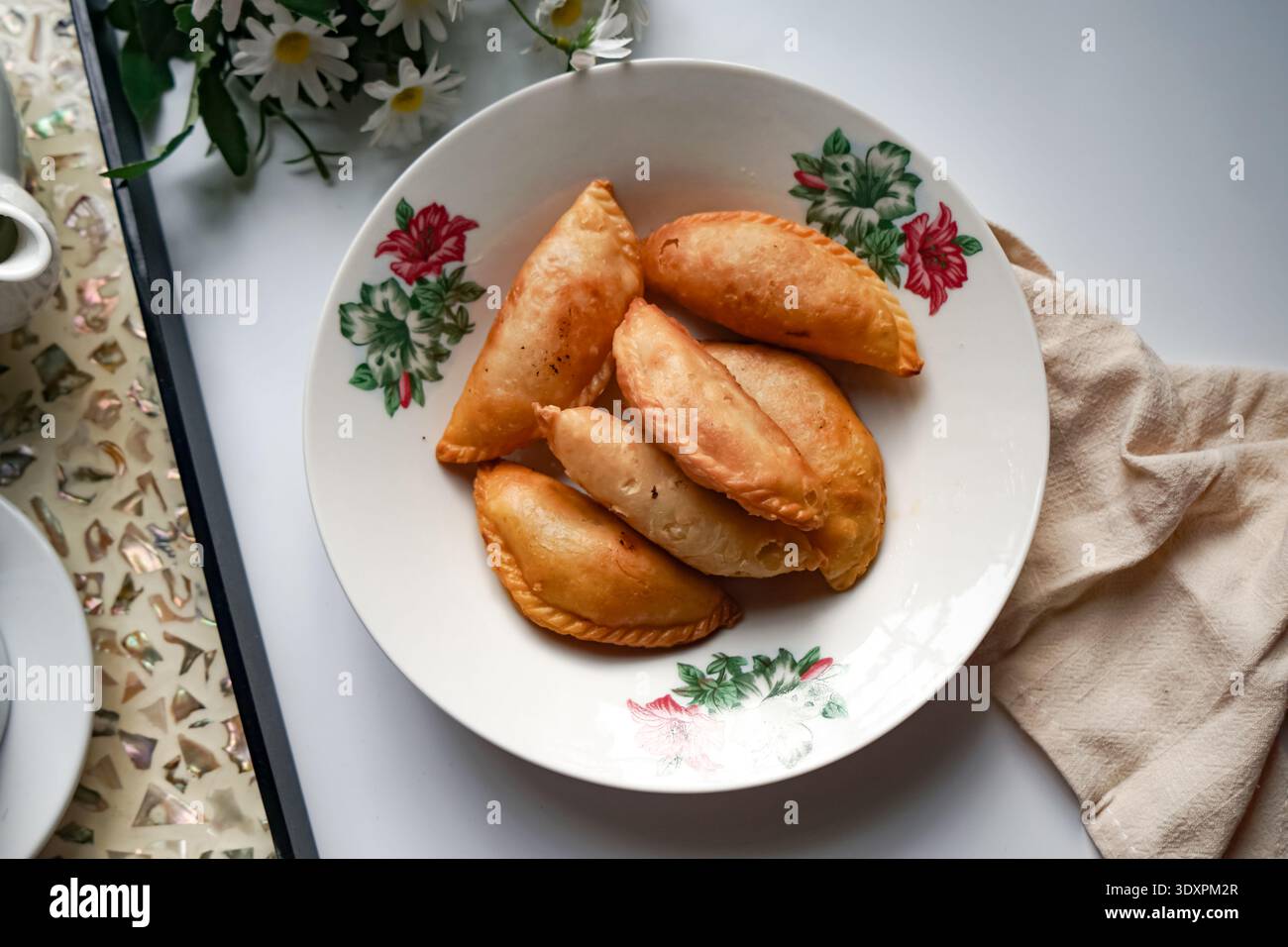 Un piatto di spugne di curry dorate con set da tè e margherite su sfondo bianco. Foto Stock
