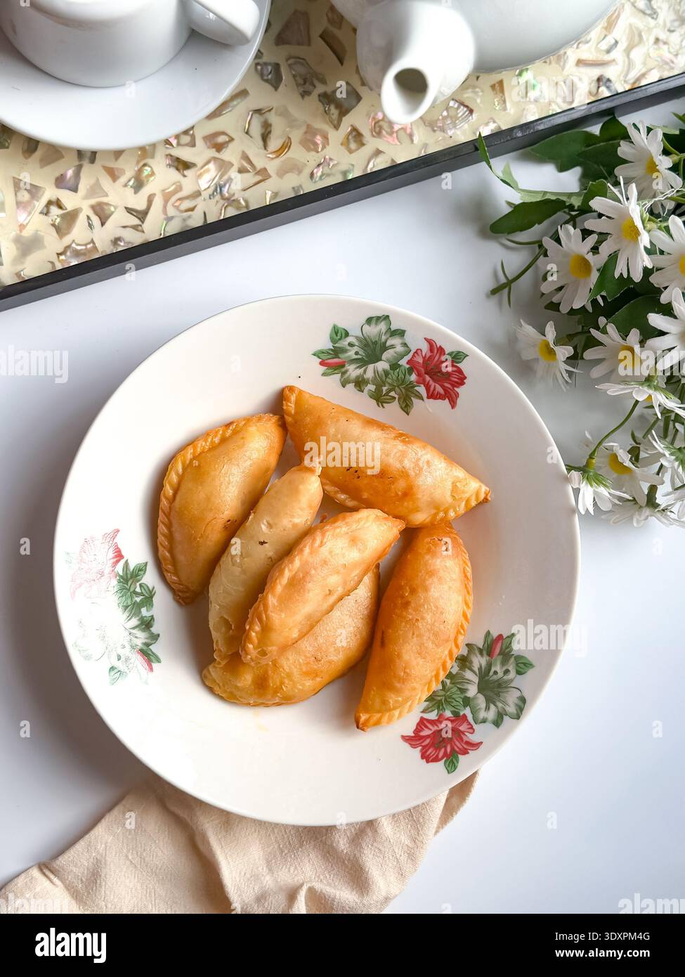 Un piatto di spugne di curry dorate con set da tè e margherite su sfondo bianco. Foto Stock