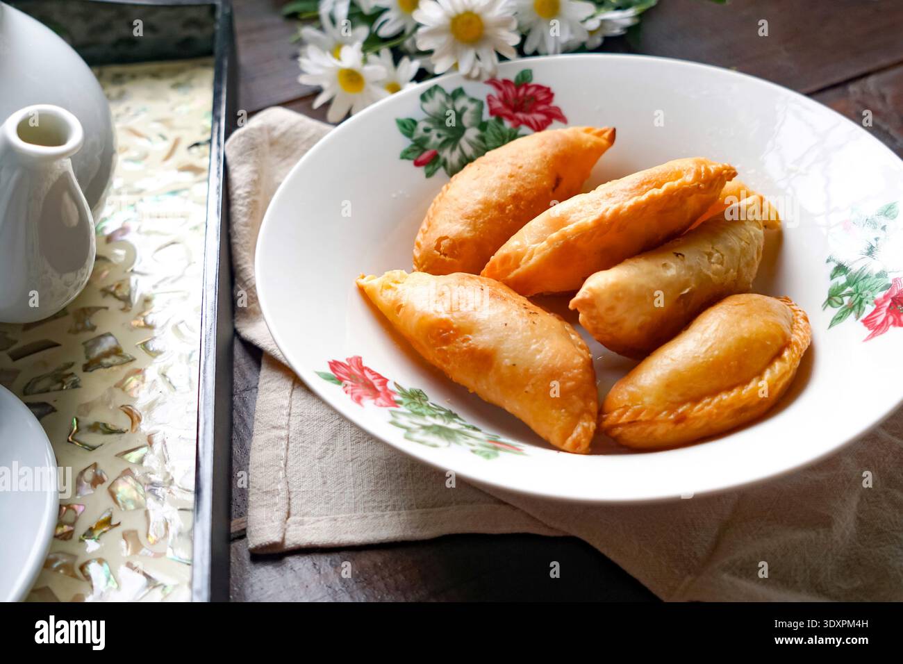 Un piatto di spugne di curry dorate con set da tè rustico e margherite su fondo in legno. Foto Stock