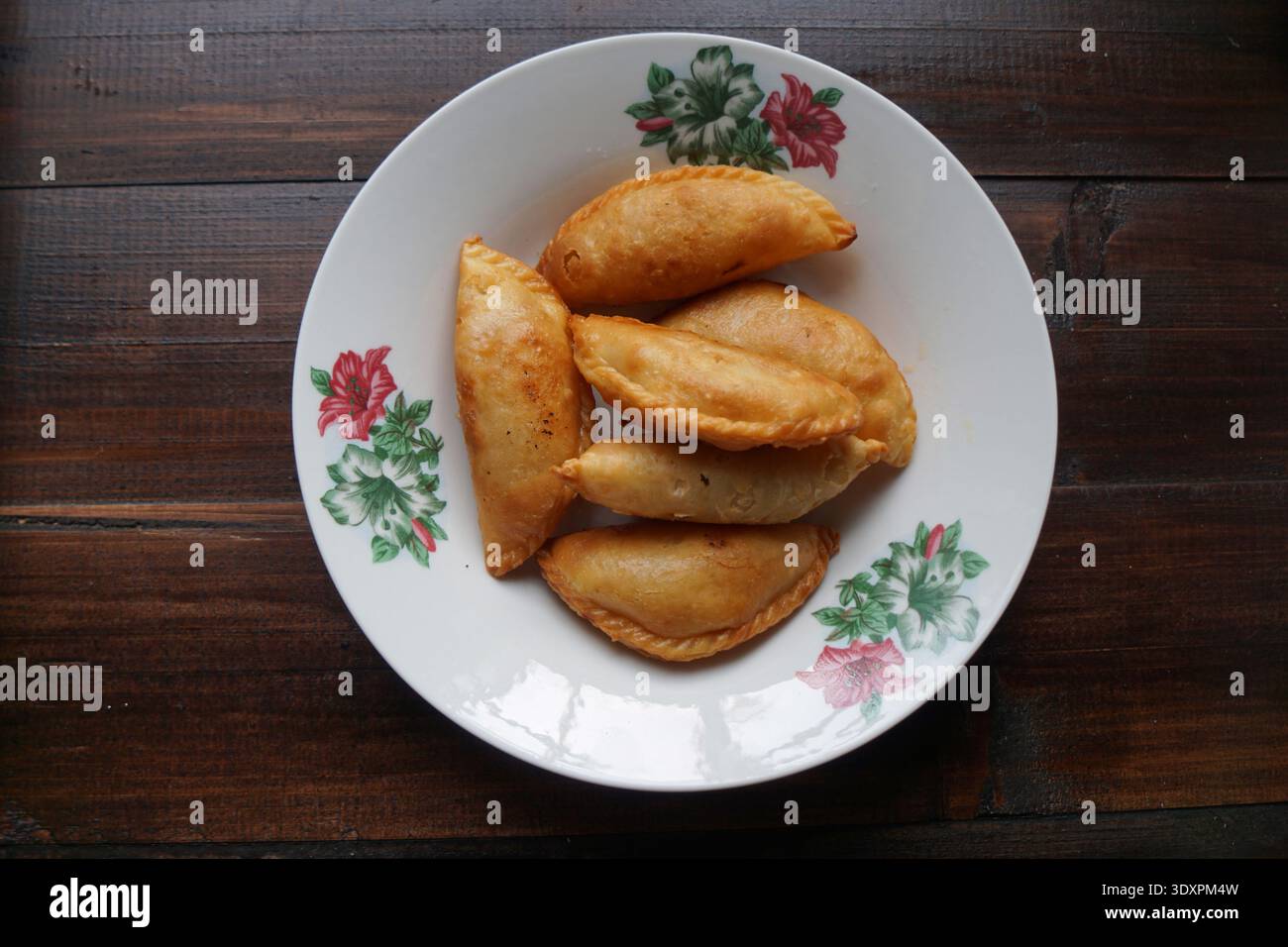 Sei spugne di curry dorate disposte su un piatto floreale su sfondo di legno scuro. Foto Stock