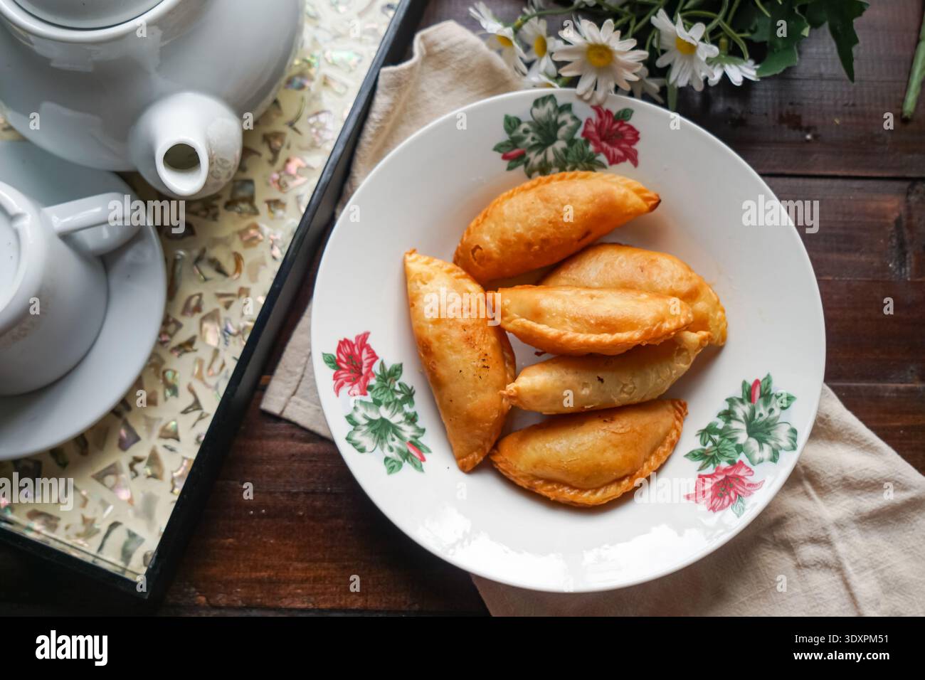Un piatto di spugne di curry dorate con set da tè rustico e margherite su fondo in legno. Foto Stock