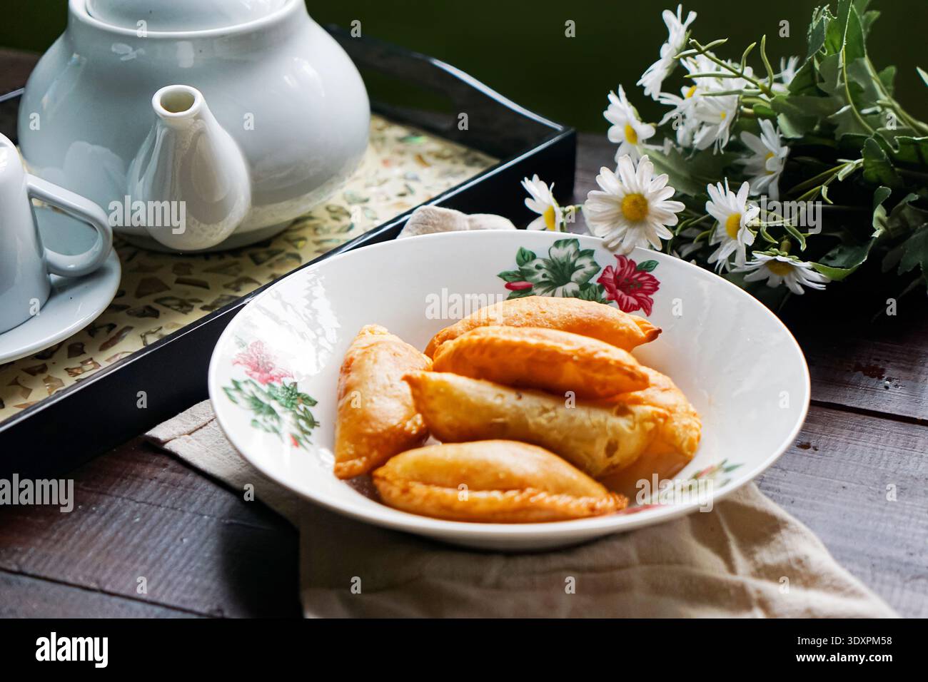 Un piatto di spugne di curry dorate con set da tè rustico e margherite su fondo in legno. Foto Stock