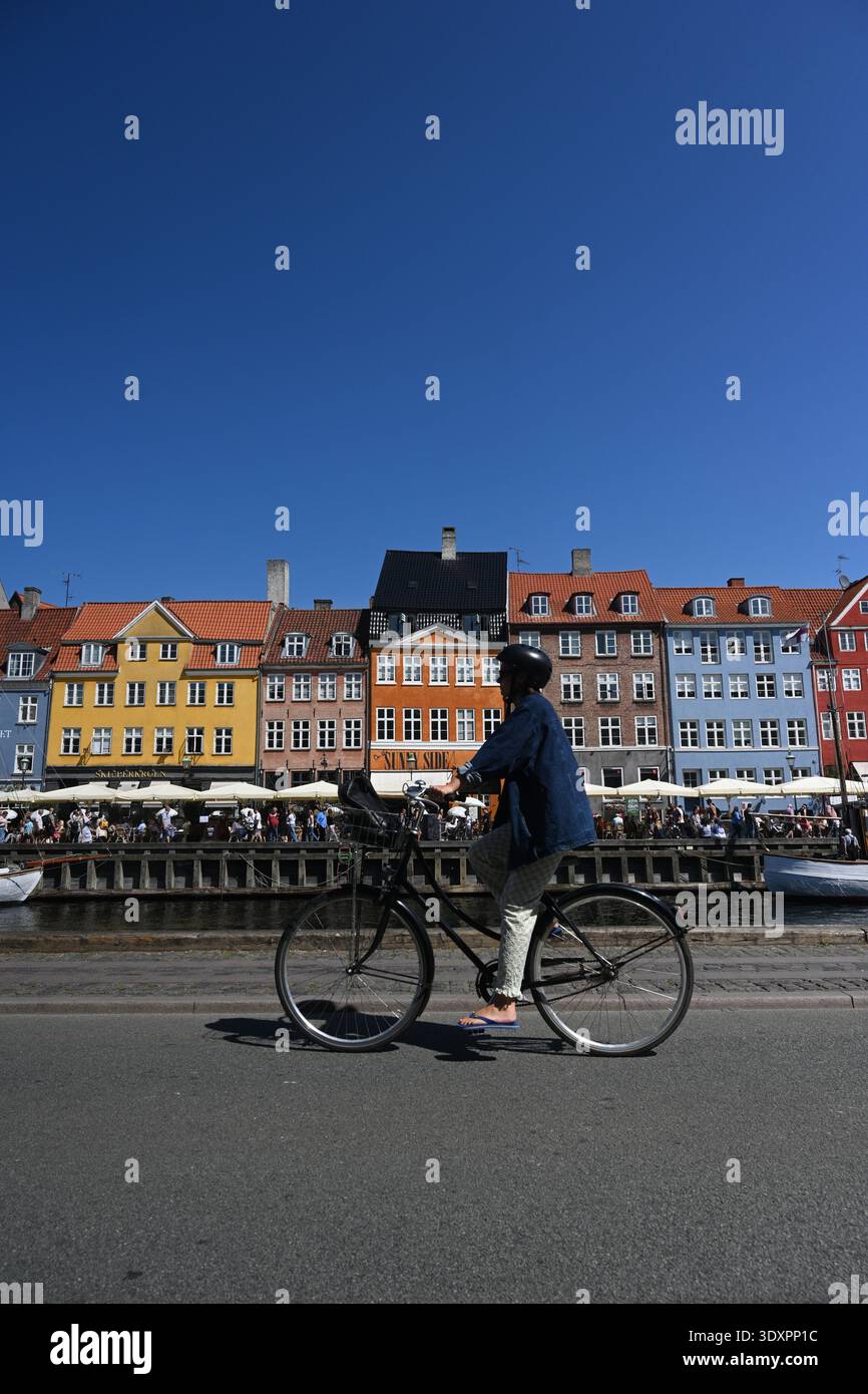 Copenaghen, Danimarca - 1 agosto 2024: Un ciclista sul lungomare di New Harbour (Nyhavn), canale e quartiere dei divertimenti a Copenaghen, Danimarca. Foto Stock