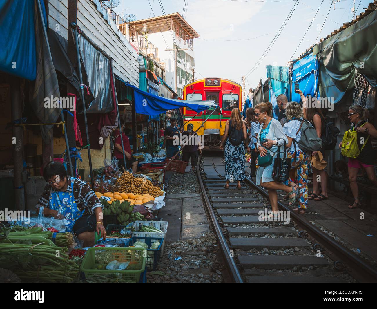 Il treno passa attraverso il mercato ferroviario di Maeklong a Samut Songkhram, Thailandia, mentre venditori e turisti si allontanano dai binari ferroviari. Foto Stock