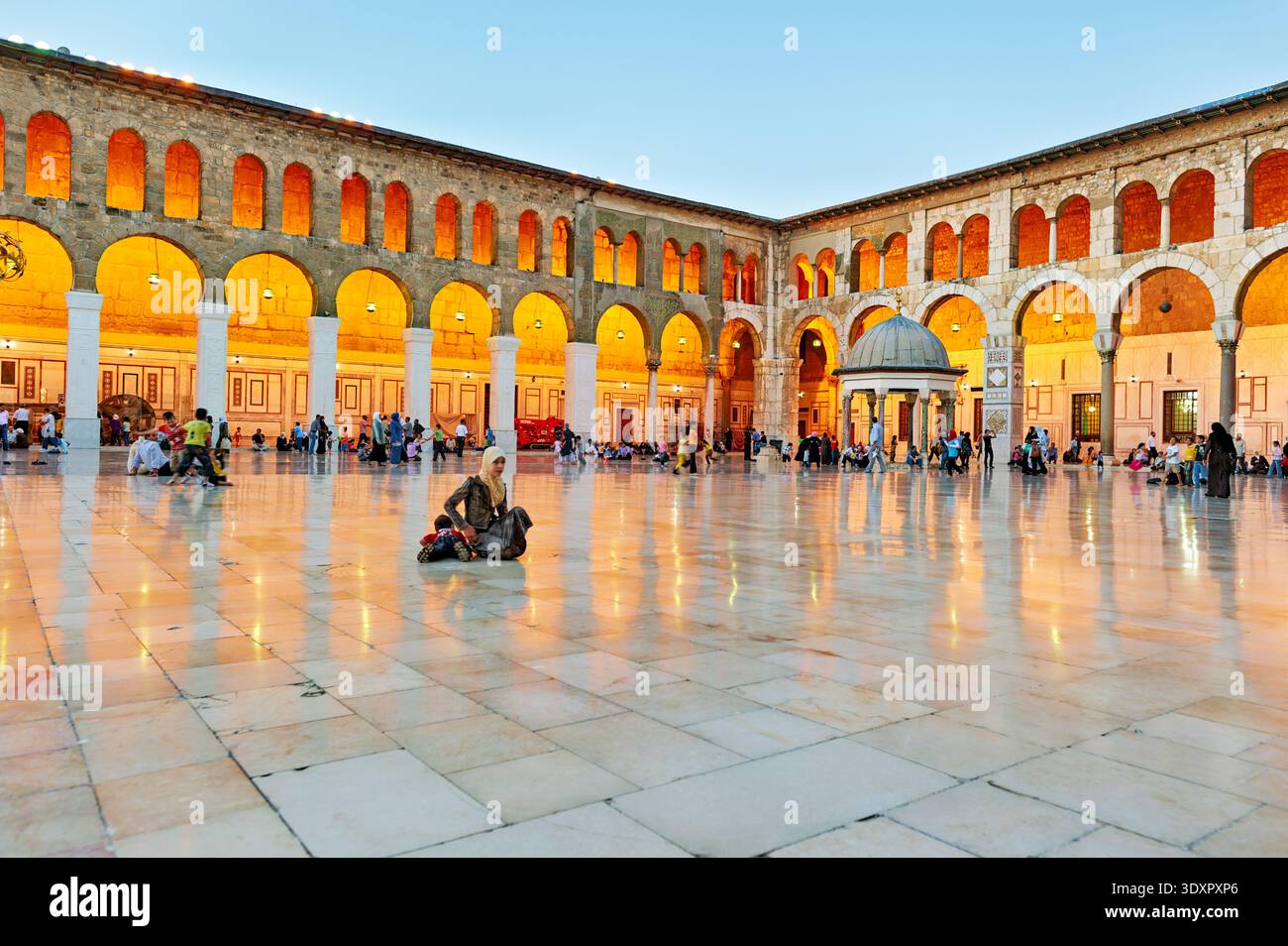 Le persone si rilassano e socializzano nell'ampio cortile della Moschea Omayyade a Damasco. Il sole tramonta e le luci iniziano a brillare. Foto Stock