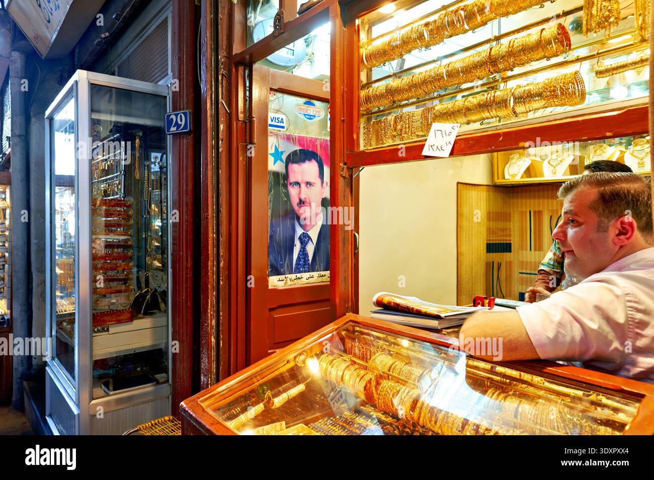 La gente esplora il suq di al-Hamidiyah a Damasco, curiosando tra i negozi di merci. Un grande ritratto dell'ex presidente Assad è appeso al muro accanto a un venditore. Foto Stock