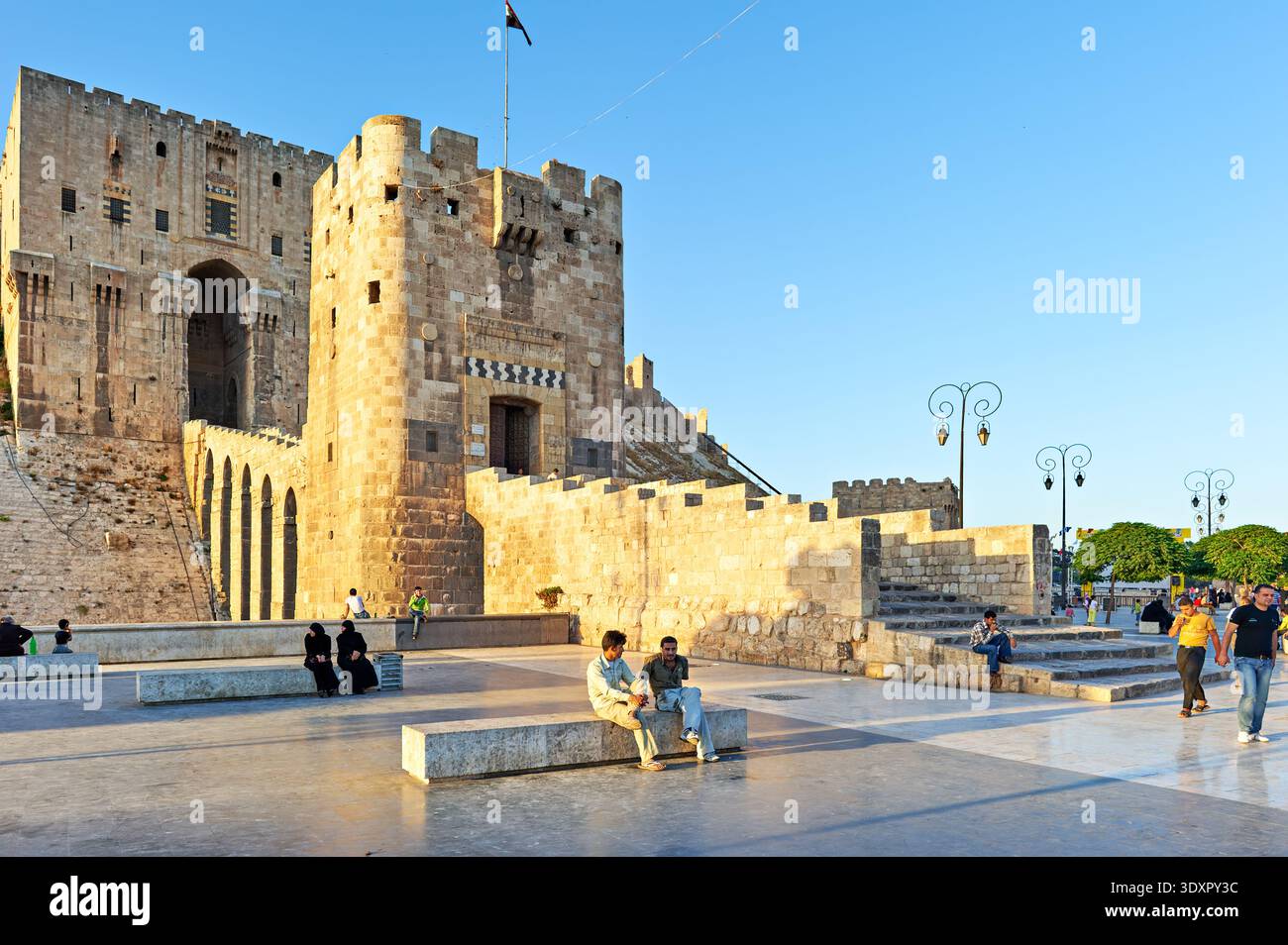 La gente si riunisce vicino alla Cittadella di Aleppo in Siria. Il sole tramonta, creando un caldo bagliore sulle antiche pietre. Foto Stock