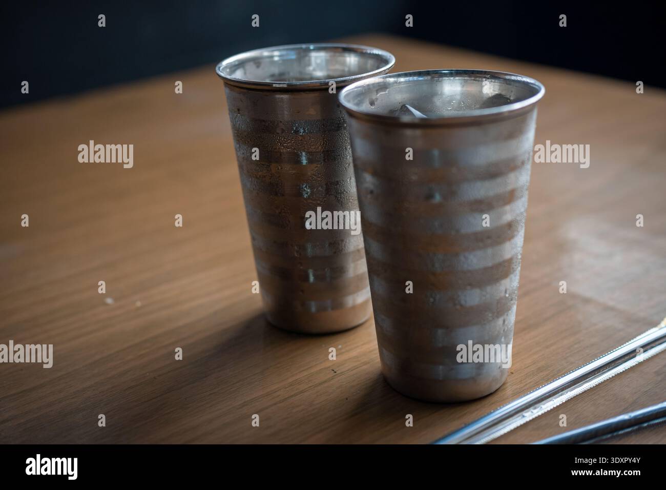 Due bicchieri in metallo freddo e cannucce d'argento su una superficie di legno Foto Stock