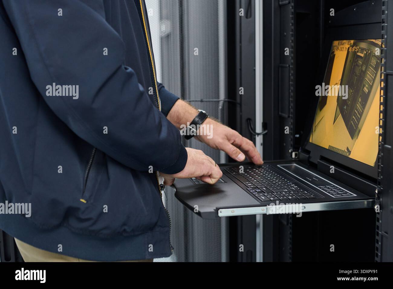 Tecnico IT che utilizza un laptop montato su rack per monitorare i server durante la manutenzione in un data center Foto Stock
