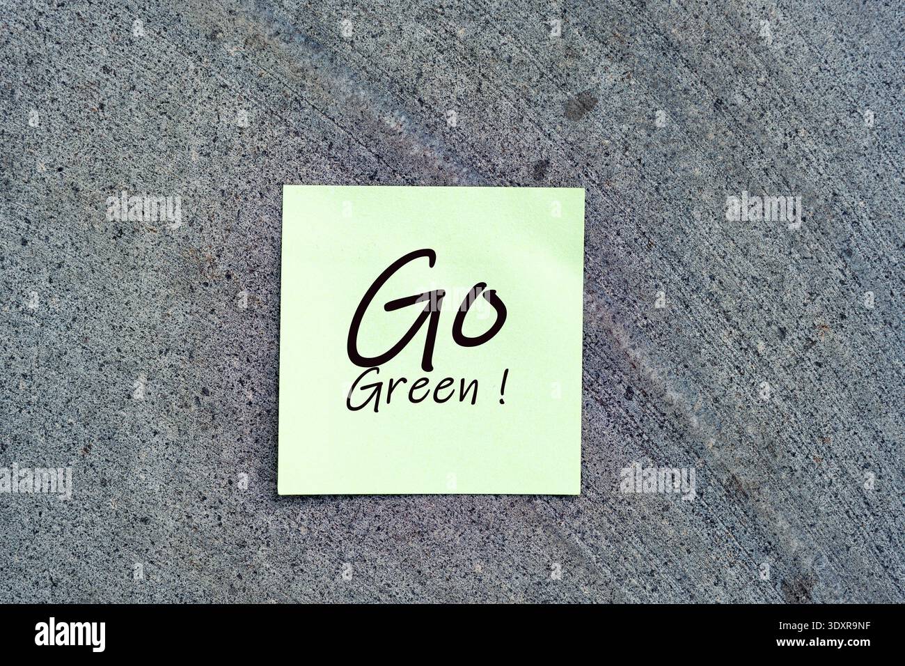 Una nota adesiva verde chiaro con il testo scritto a mano "Go Green!" posizionato su una superficie di pietra grigia, che rappresenta la consapevolezza ambientale Foto Stock