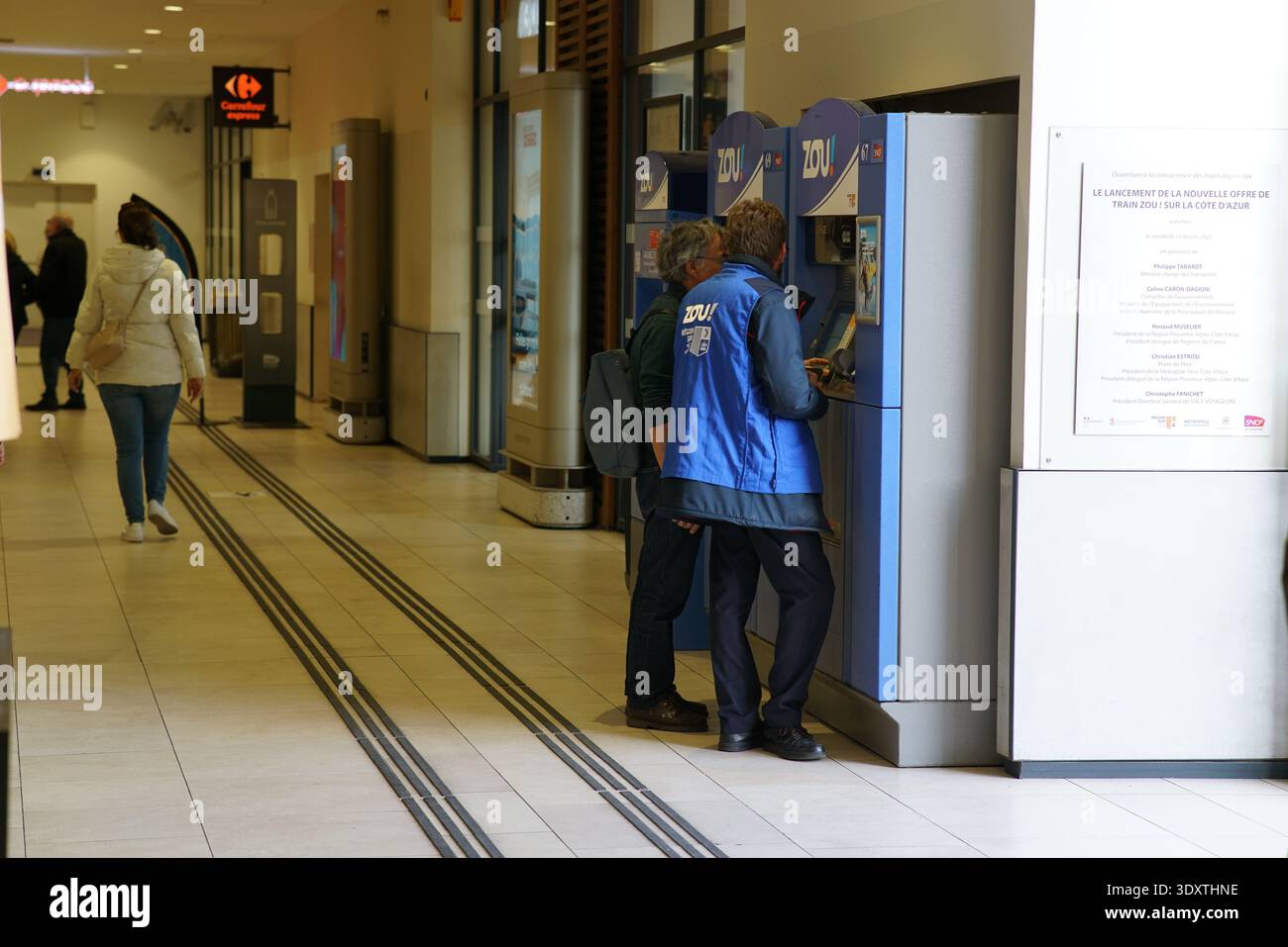 I viaggiatori interagiscono con gli armadietti blu del luminoso corridoio della stazione ferroviaria di Nice Ville, con personale disponibile in gilet blu che assiste.Nizza Foto Stock