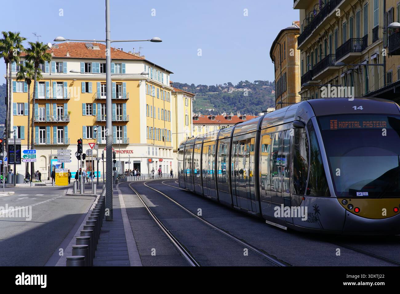 Moderna linea 14 del tram che conduce all'ospedale Pasteur passando per una strada costeggiata da palme con edifici gialli a Nizza in Francia sotto il cielo blu. Nizza, Francia Foto Stock