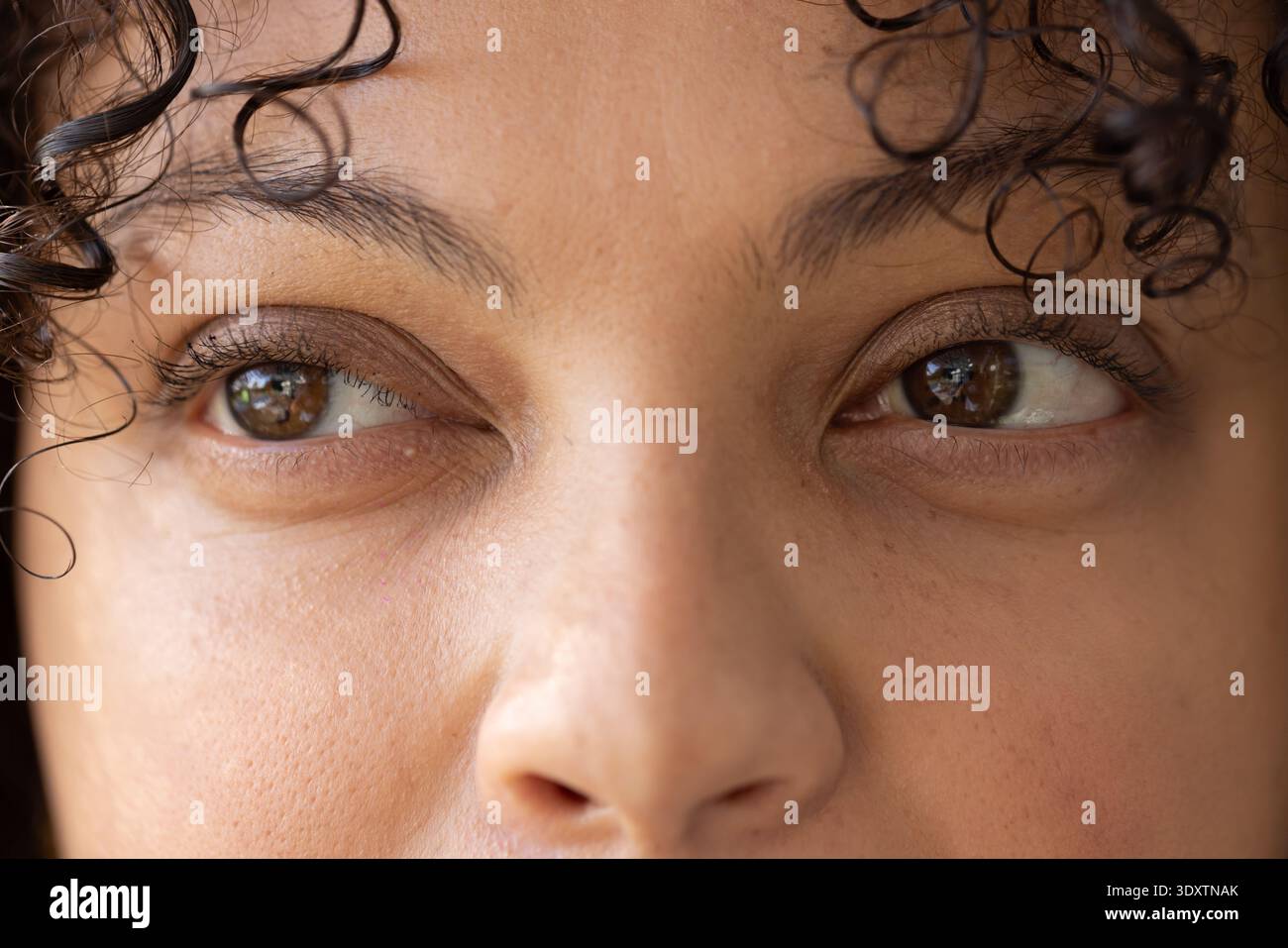 Donna che si concentra sull'area degli occhi, che guarda leggermente a destra nella stanza con riflessi e ricci della finestra Foto Stock