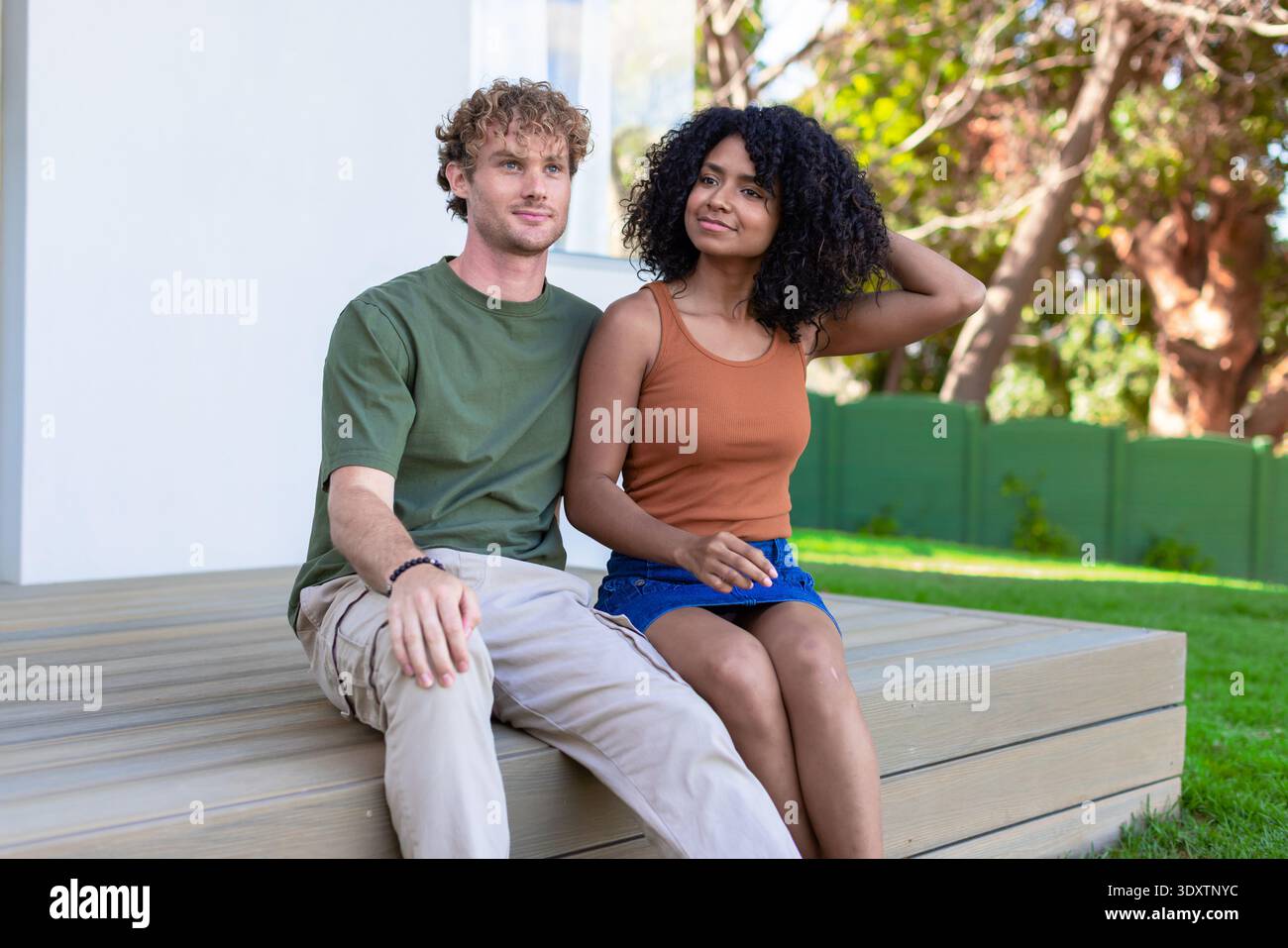 Coppia seduta sul ponte di legno a casa, indossa T-shirt verde e canotta antiruggine Foto Stock
