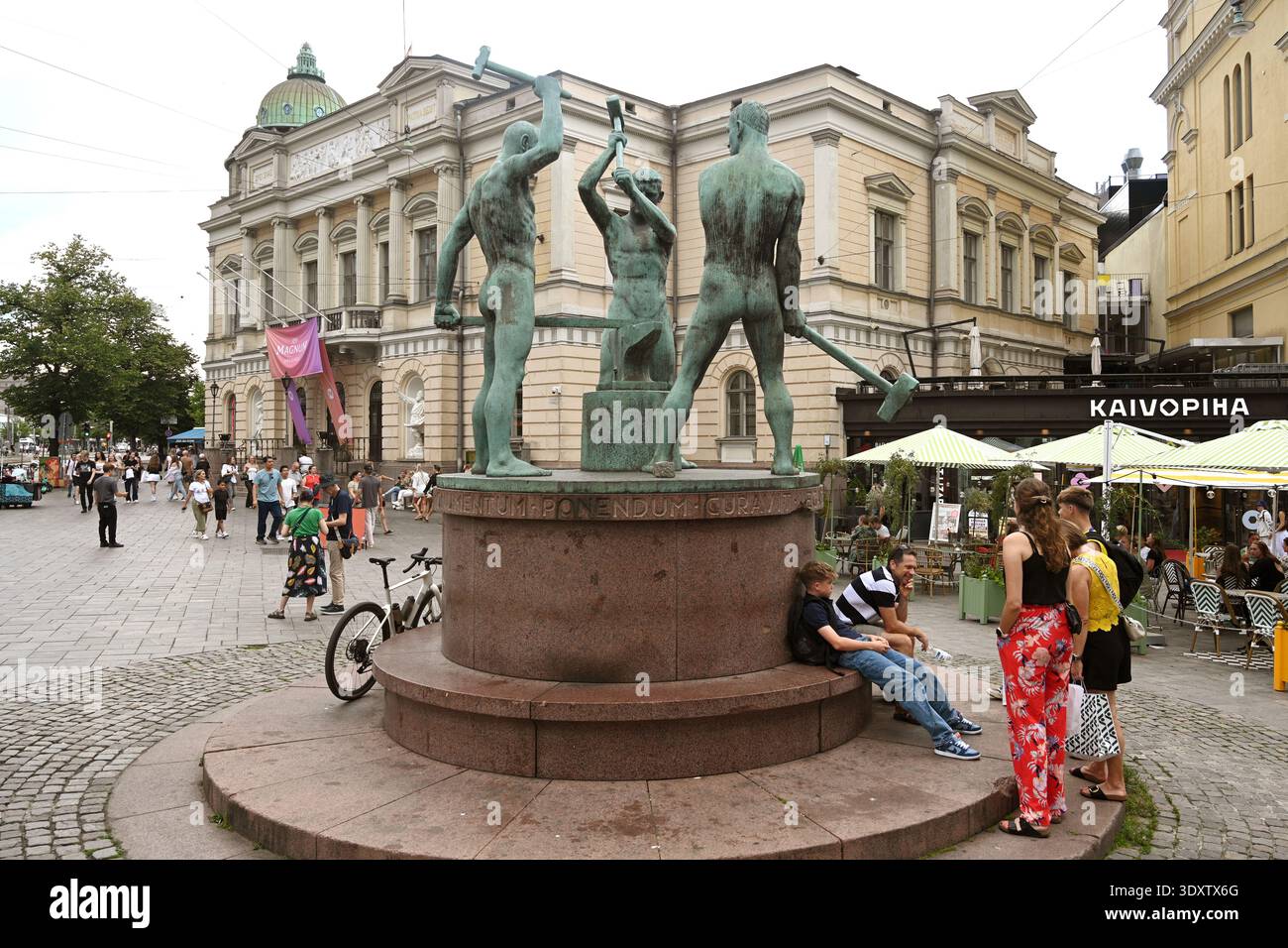 Helsinki, Finlandia - 25 luglio 2024: Un popolo vicino alla statua dei tre fabbri e alla vecchia casa degli studenti di Helsinki. Foto Stock