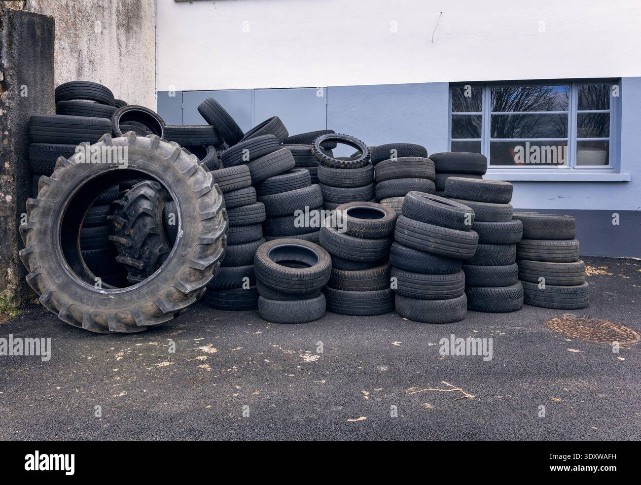 un'enorme pila di pneumatici usati per trattori e veicoli impilati su una parete industriale piana che mostra le superfici in gomma usurate e i rifiuti automobilistici per impieghi gravosi Foto Stock